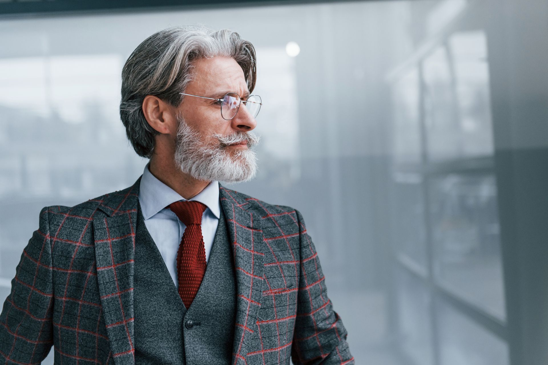 Man in checkered suit, vest, and tie, wearing glasses, looking to the side.