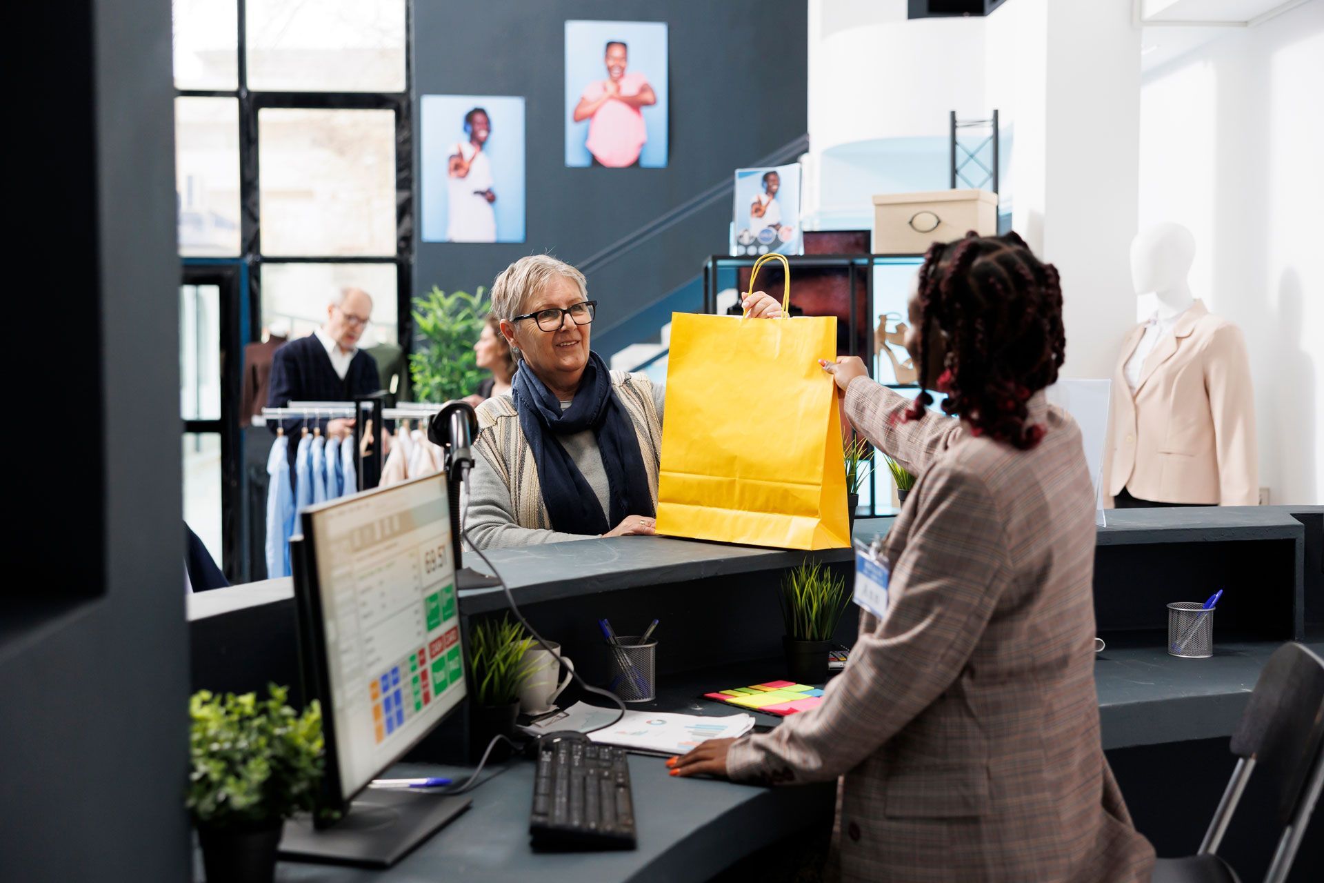Woman receiving a yellow shopping bag from a sales associate at a store's counter.