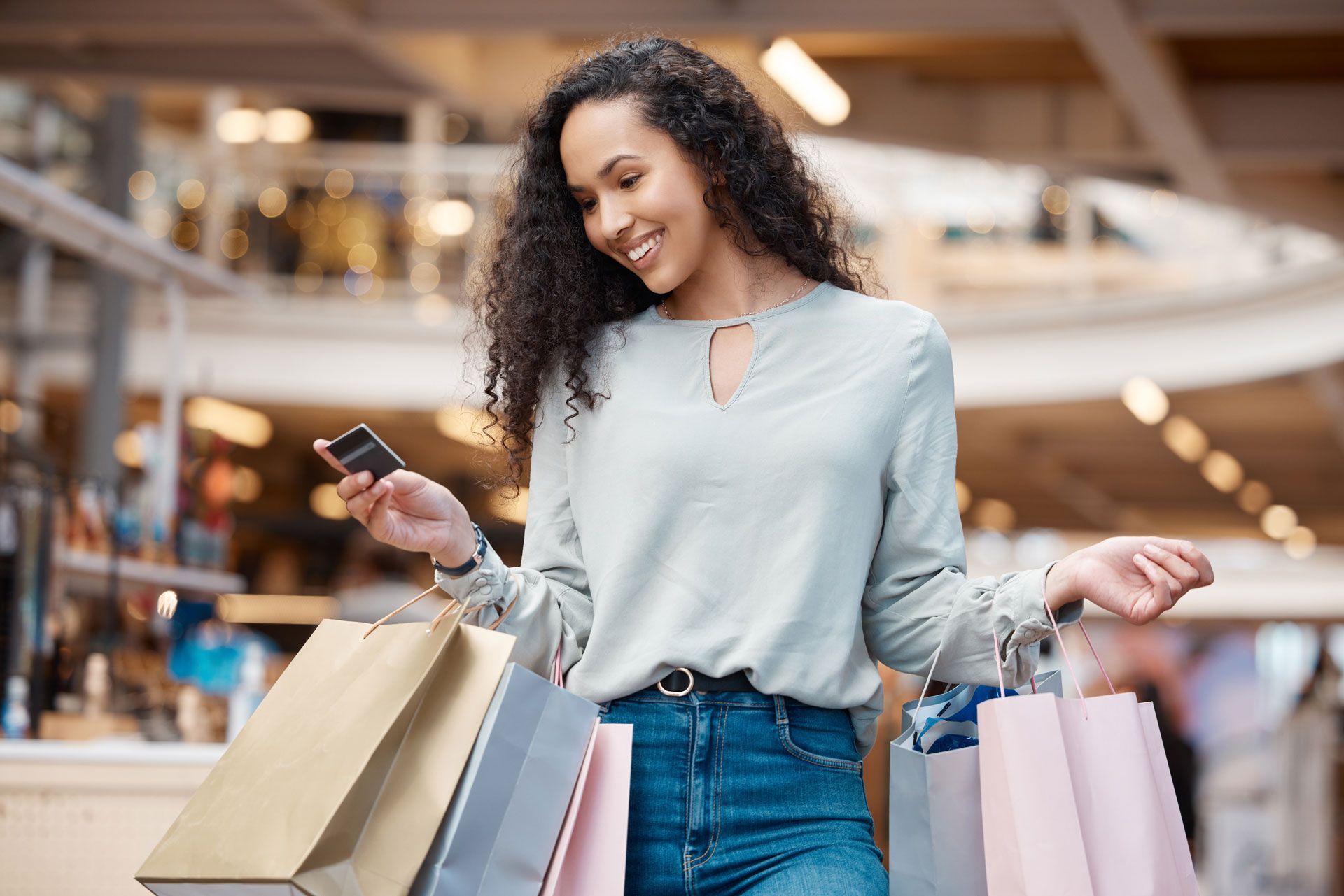 Woman holding shopping bags and a credit card, smiling in a shopping mall.