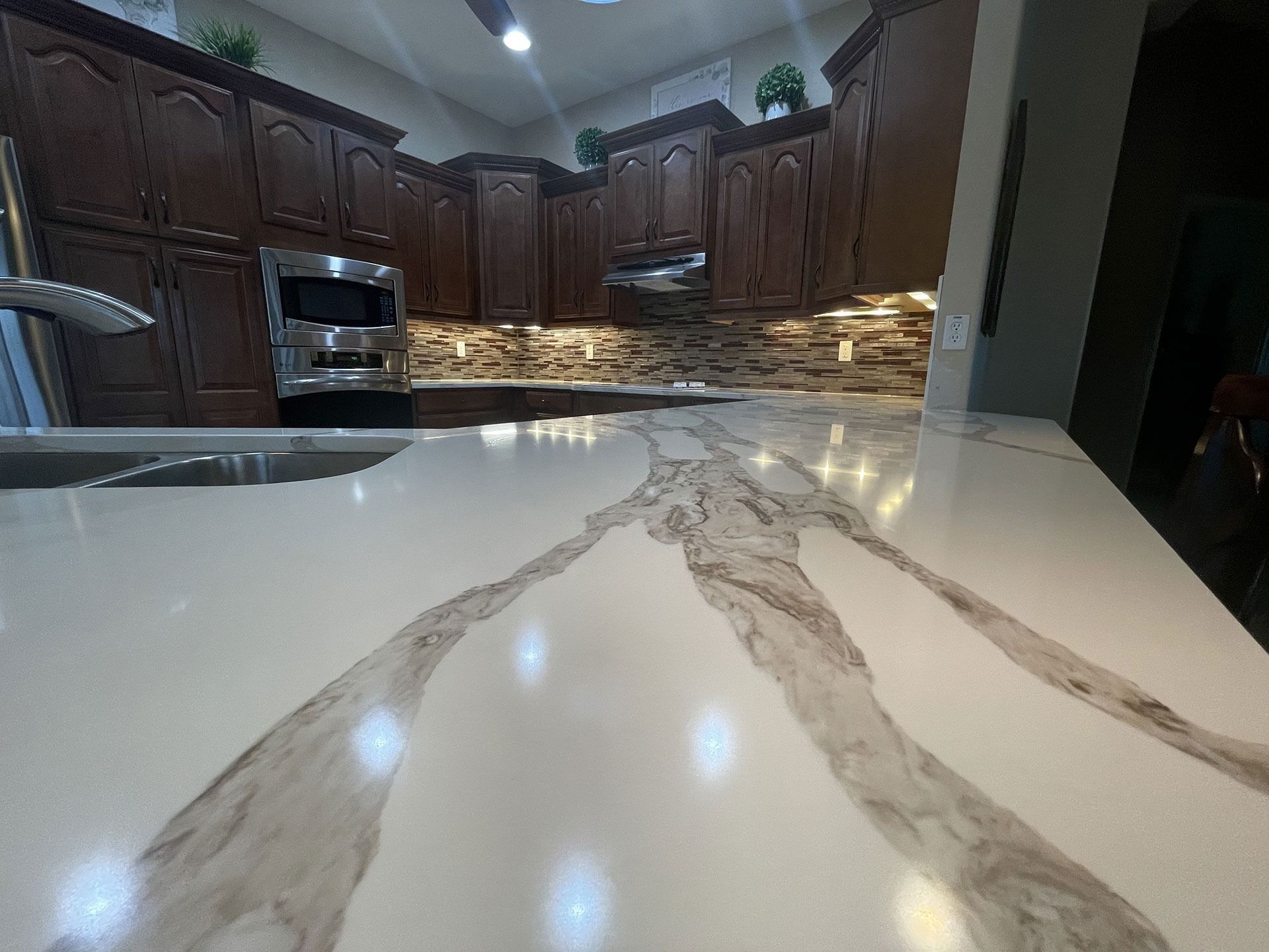 A kitchen island with a white and gray marbled countertop in front of dark wood cabinets and a stone backsplash.