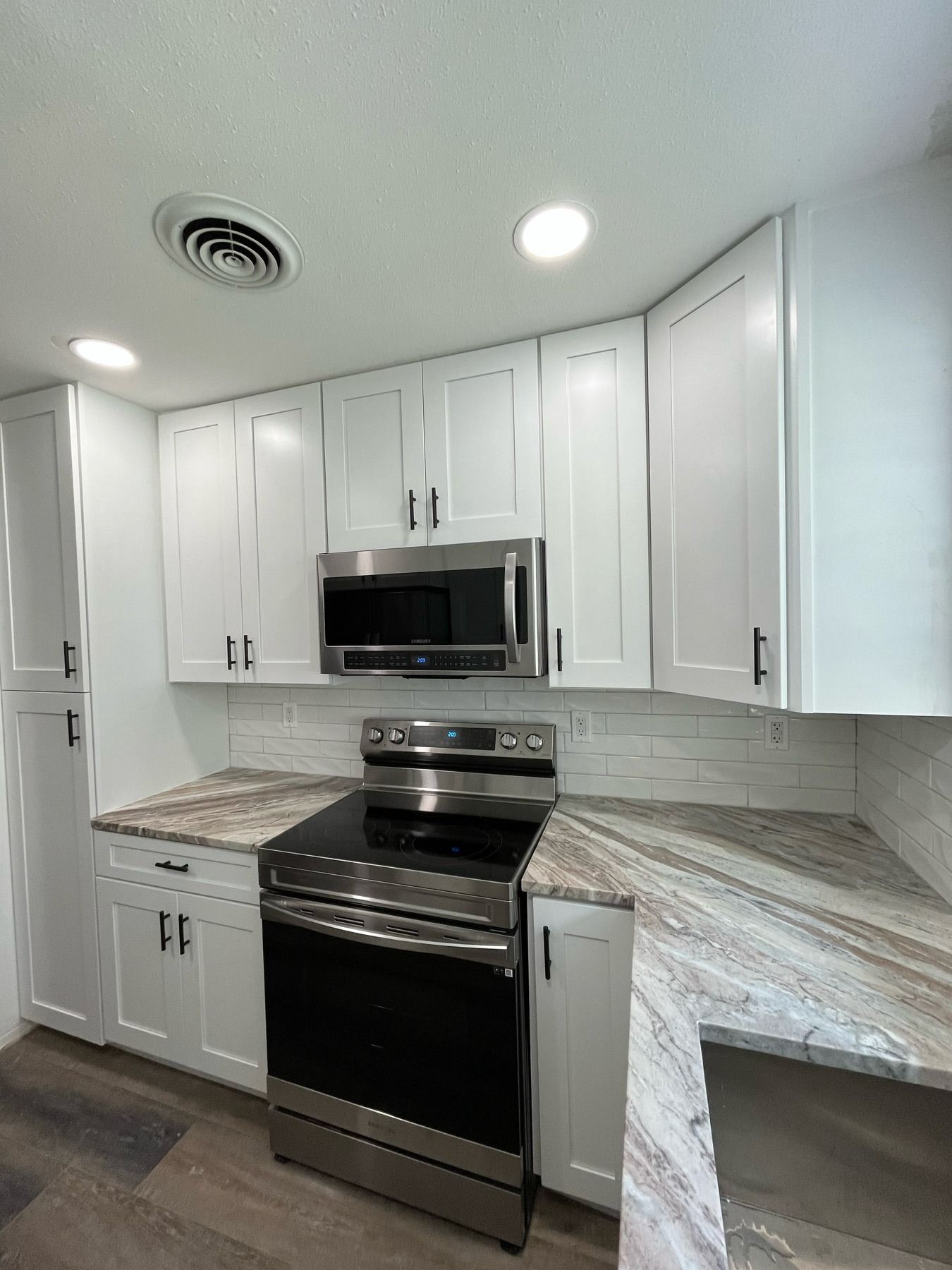 A modern kitchen with white cabinets, stainless steel appliances, and marble-patterned countertops.