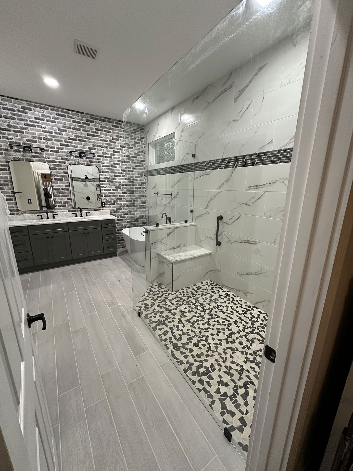 A modern bathroom featuring a walk-in shower with a pebble floor, white marble walls, and a separate vanity area.