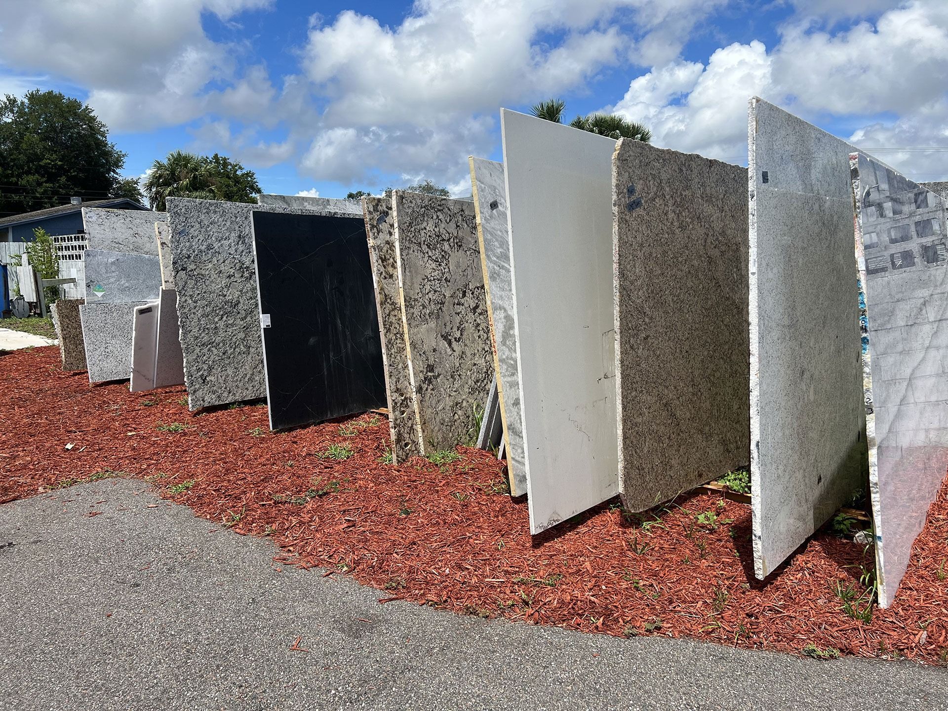 Large stone slabs of various colors and textures displayed in a row outdoors on red mulch.