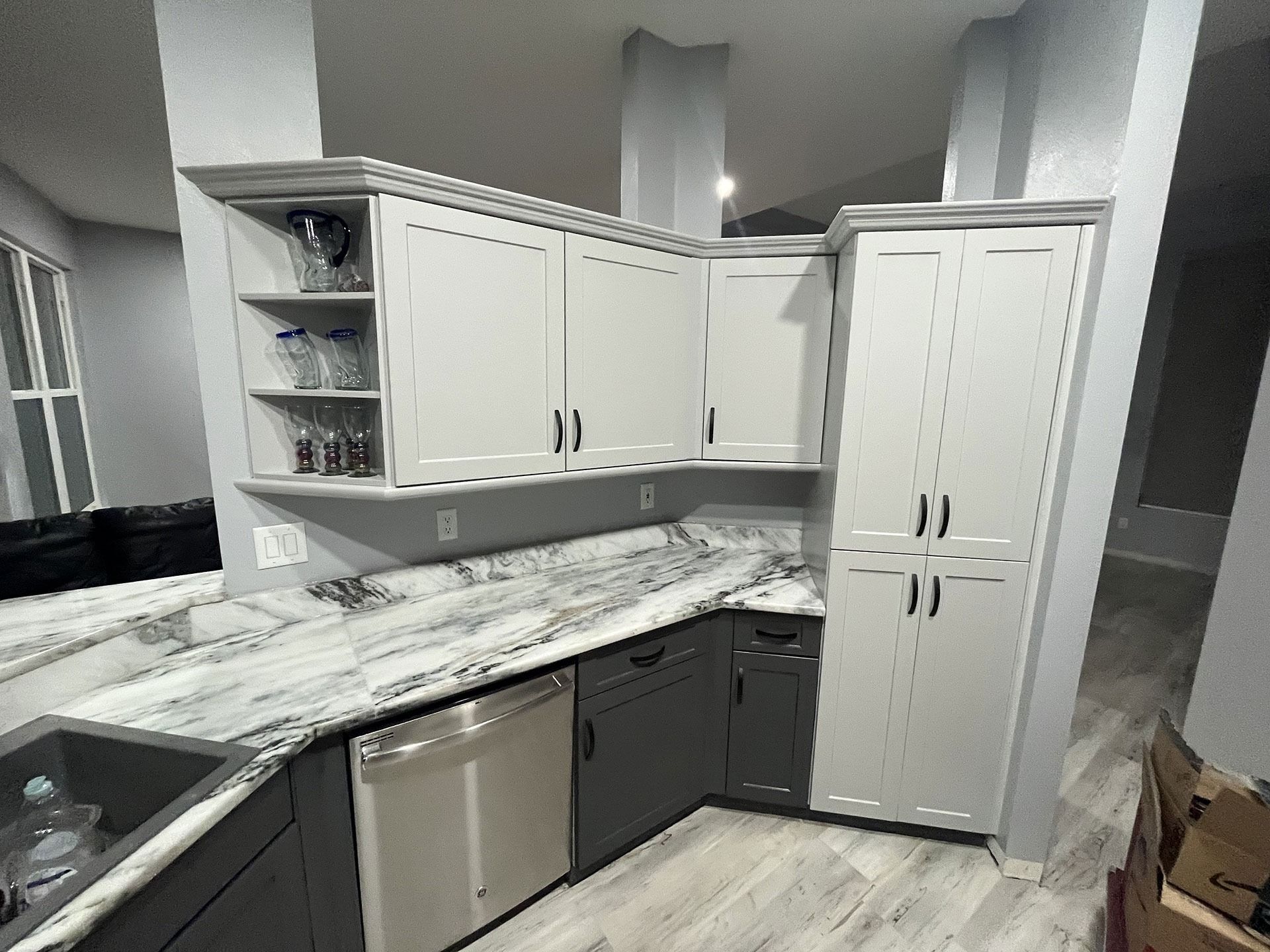 A modern kitchen featuring white cabinets, dark gray lower cabinets, and marbled countertops.