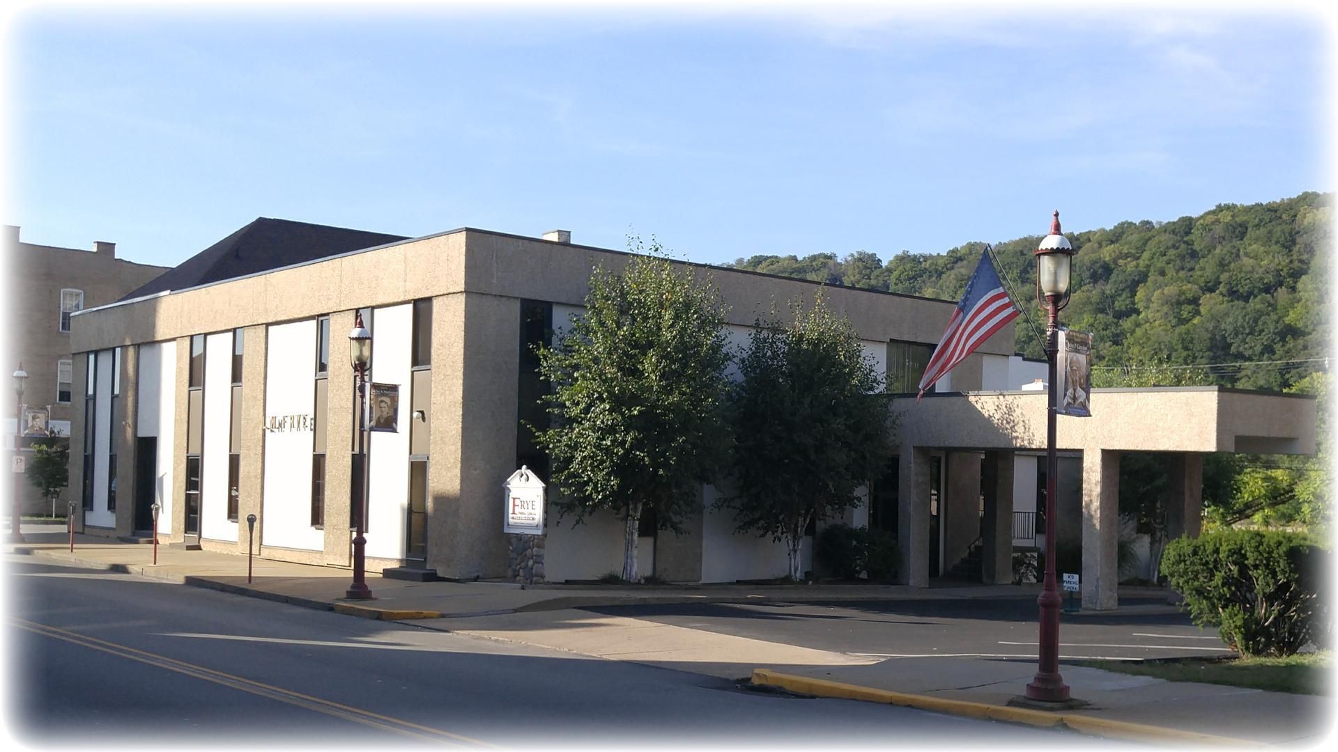 Small beige civic building on a quiet street, with an American flag and trees in the background.