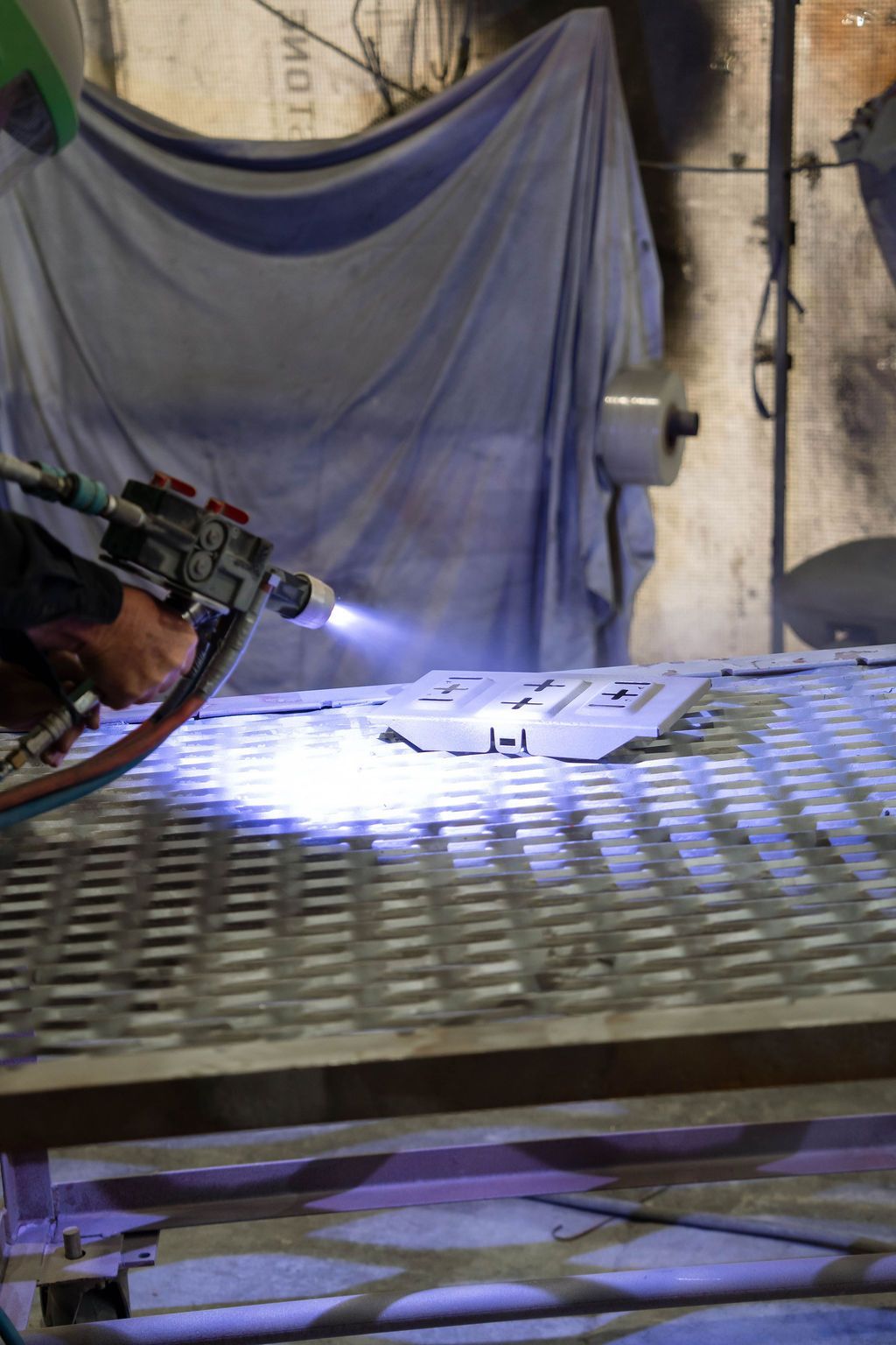 A hand uses a professional spray gun to apply a finish to a metal part on a workbench in a workshop.