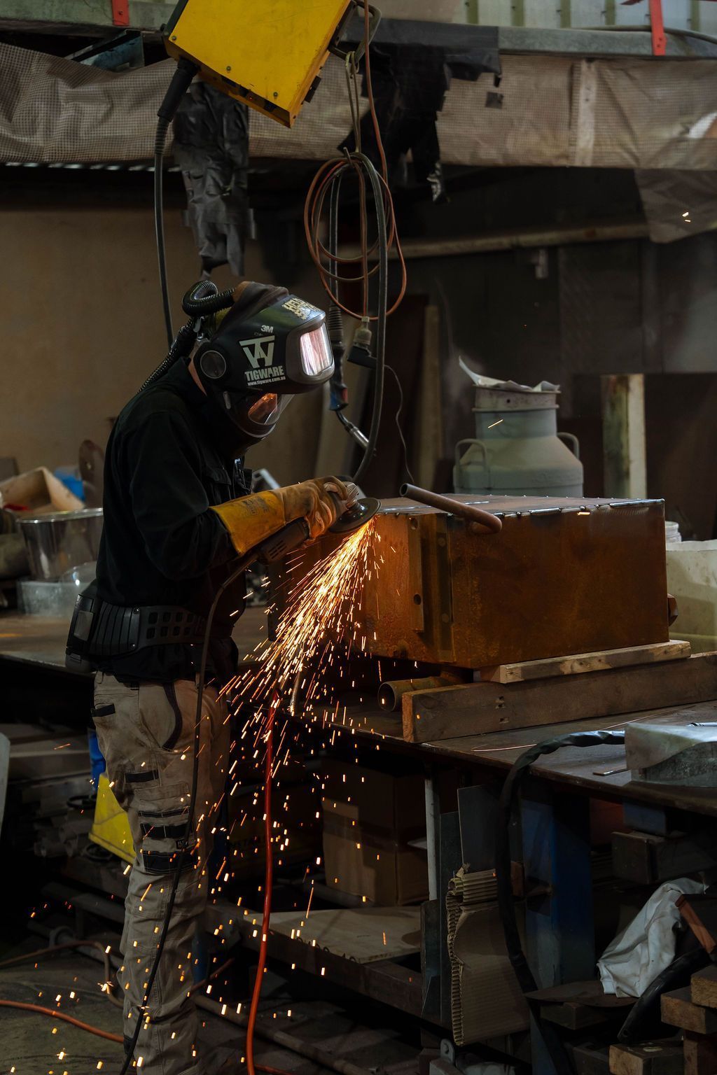 Welder in a workshop cutting metal with sparks flying from a large rust-colored box
