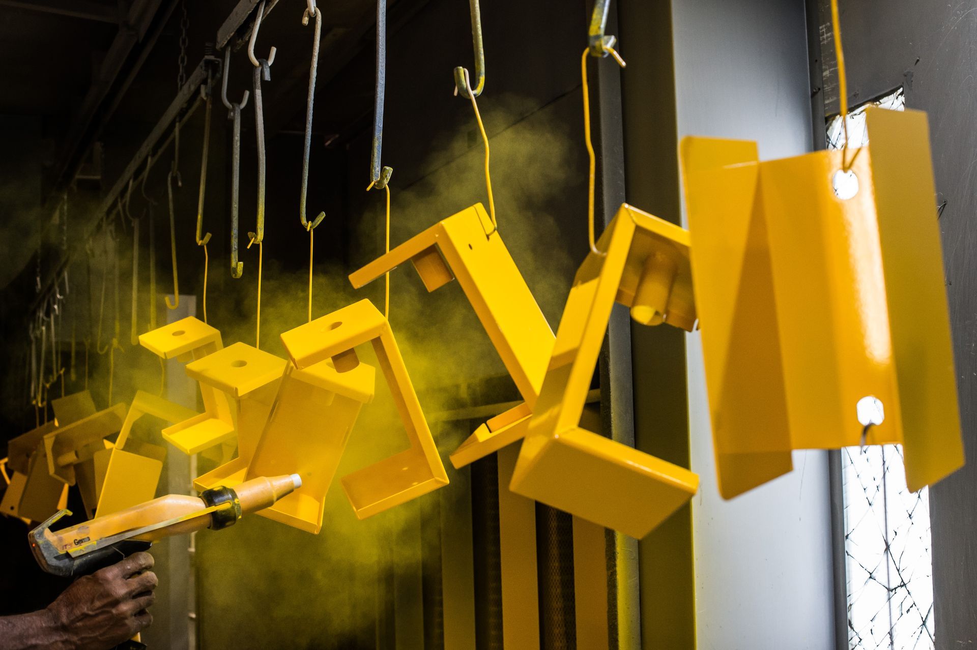 A close-up of a worker performing a powder coating service, spraying yellow powder over products. A close-up of a worker performing a powder coating service, spraying yellow powder over products.