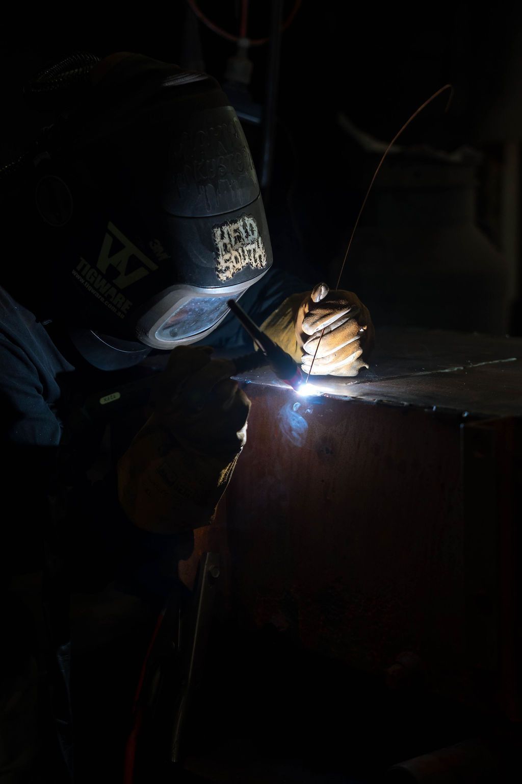 A welder in protective gear uses a torch to join metal, creating a bright spark in a dim workspace.