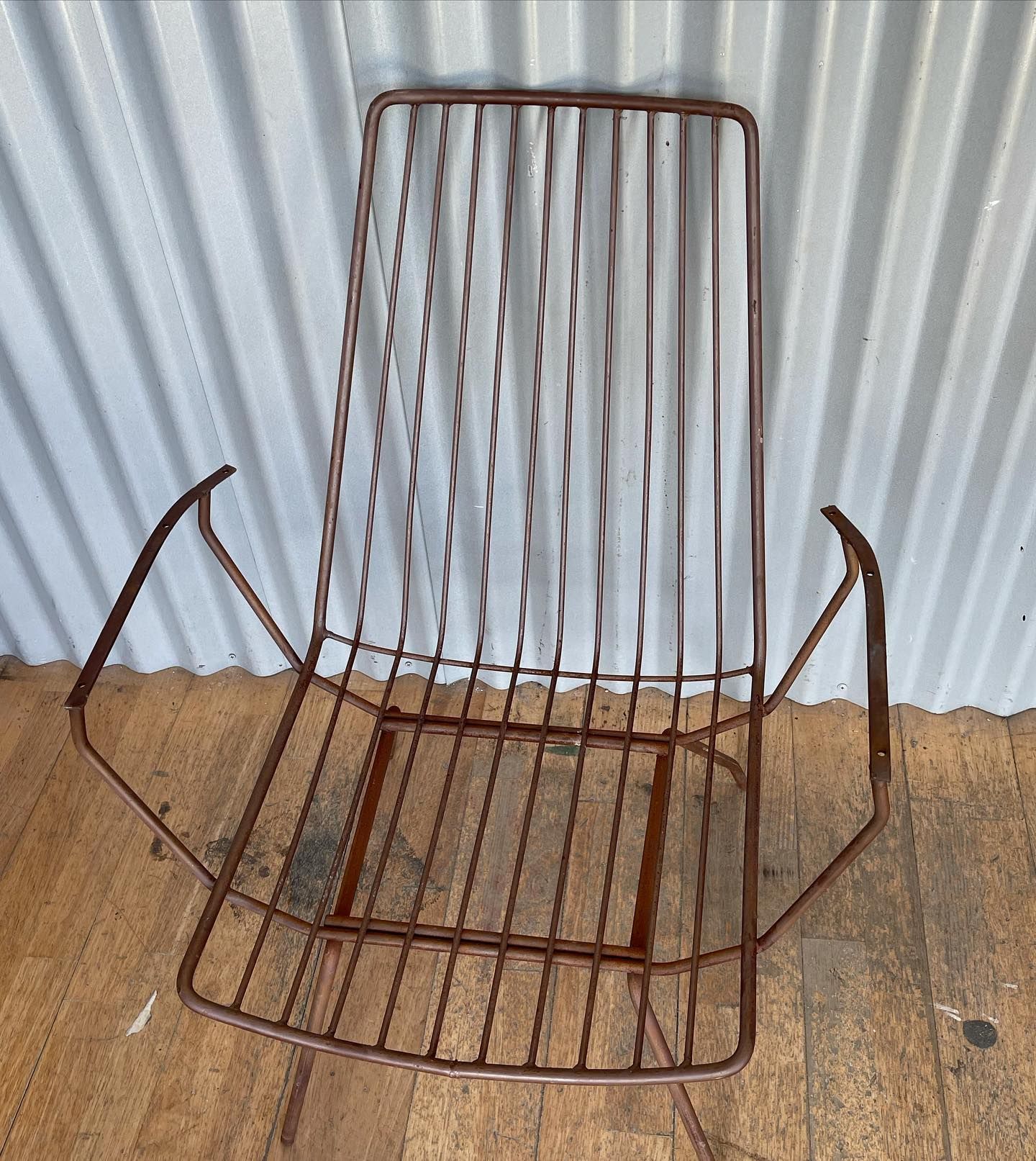 Bronze wire chair with seat and back against corrugated metal wall.