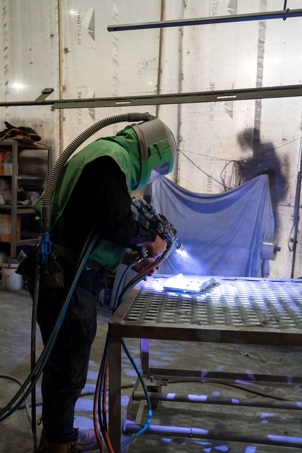 Worker in green welding gear sparks metal on a workbench in an industrial shop.