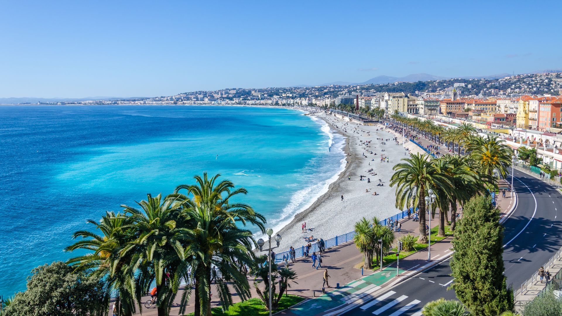 Eine Luftaufnahme eines Strandes mit Palmen und einer Stadt im Hintergrund.