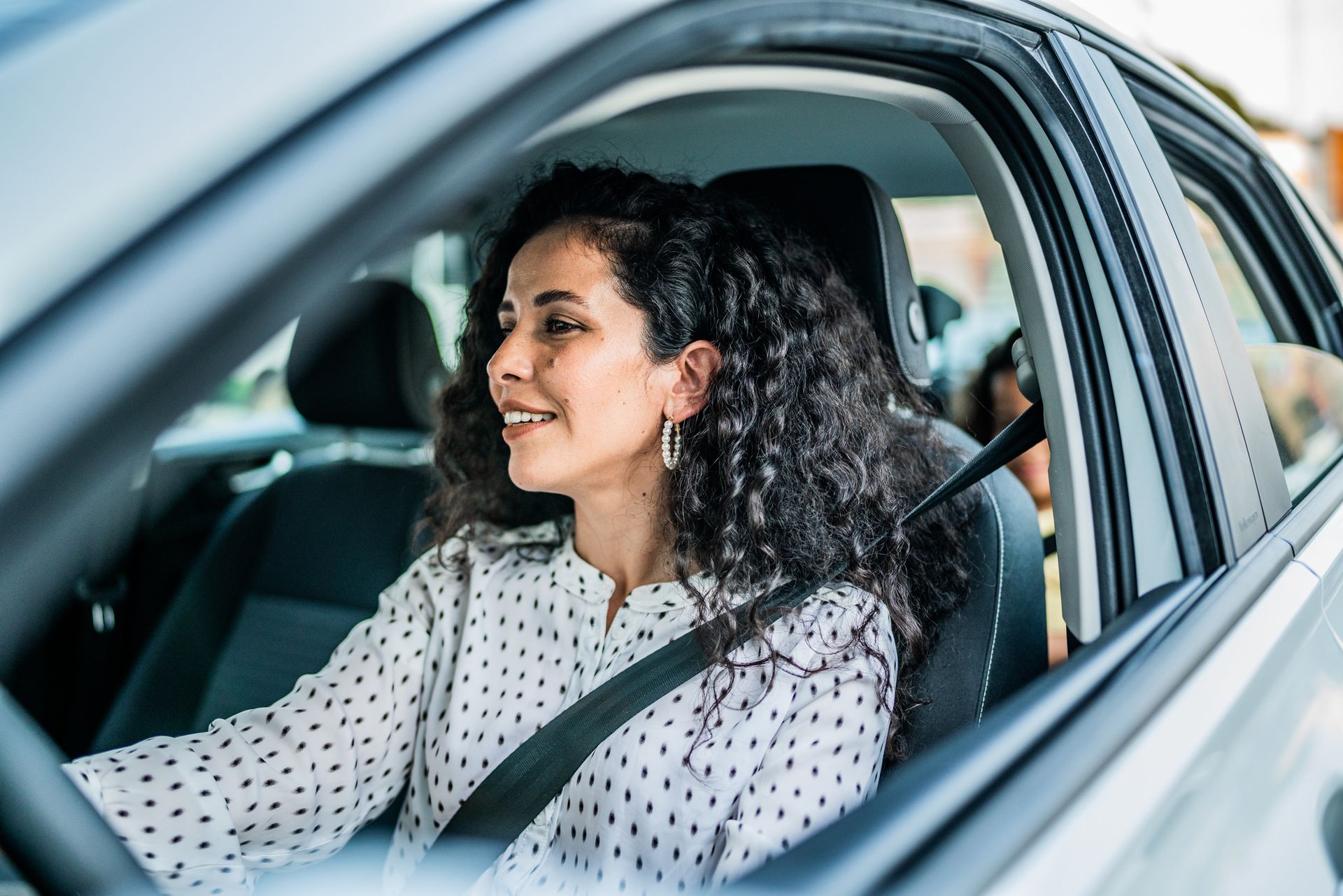 Woman driving a car, smiling, wearing a seatbelt.