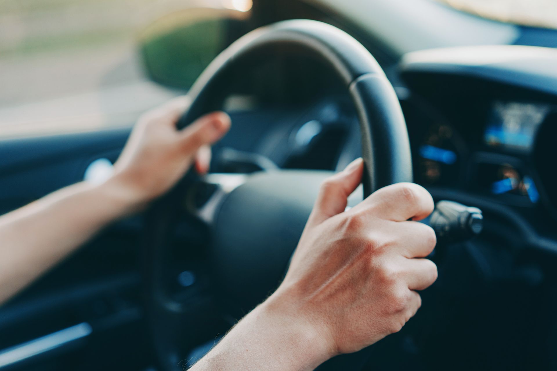 Hands gripping a black steering wheel inside a car, driving.