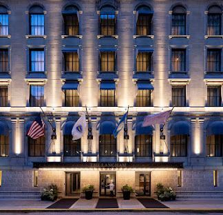 Hotel facade with arched windows, awnings, flags, and illuminated entrance.