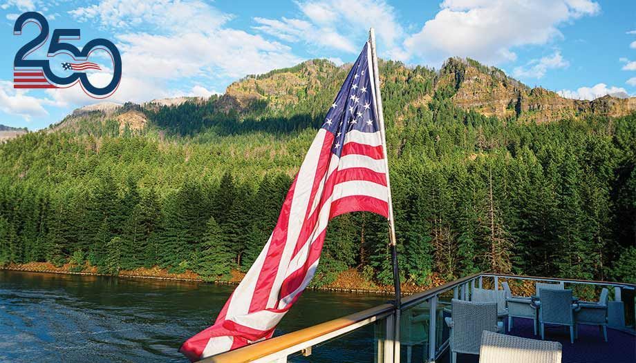 American flag on a boat deck with forested mountains and lake in the background; “250” logo in corner