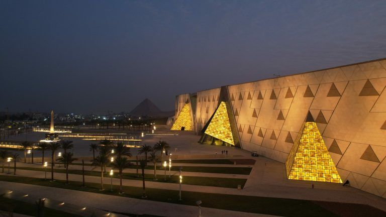 Statue of pharaoh with hieroglyphics; golden wall with rectangular pattern.