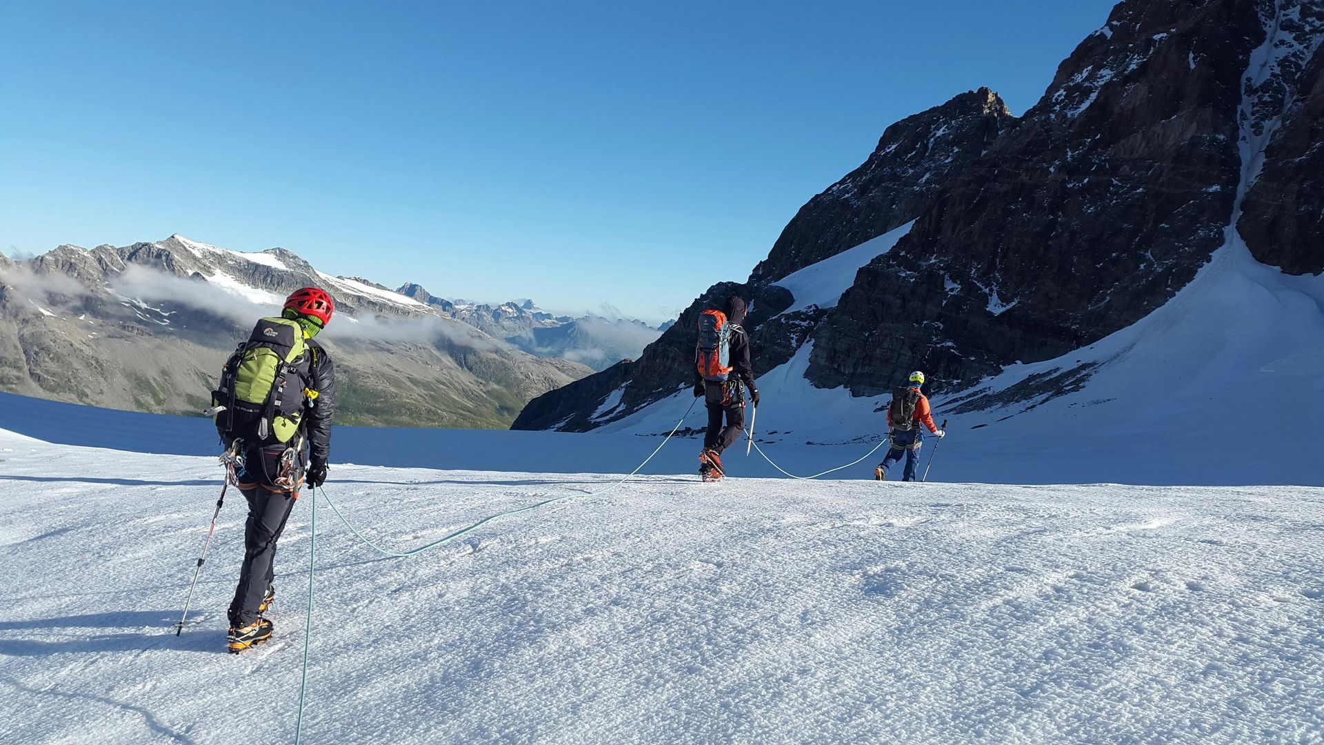 Skiers traversing a snowy mountain glacier with rocky peaks in the background