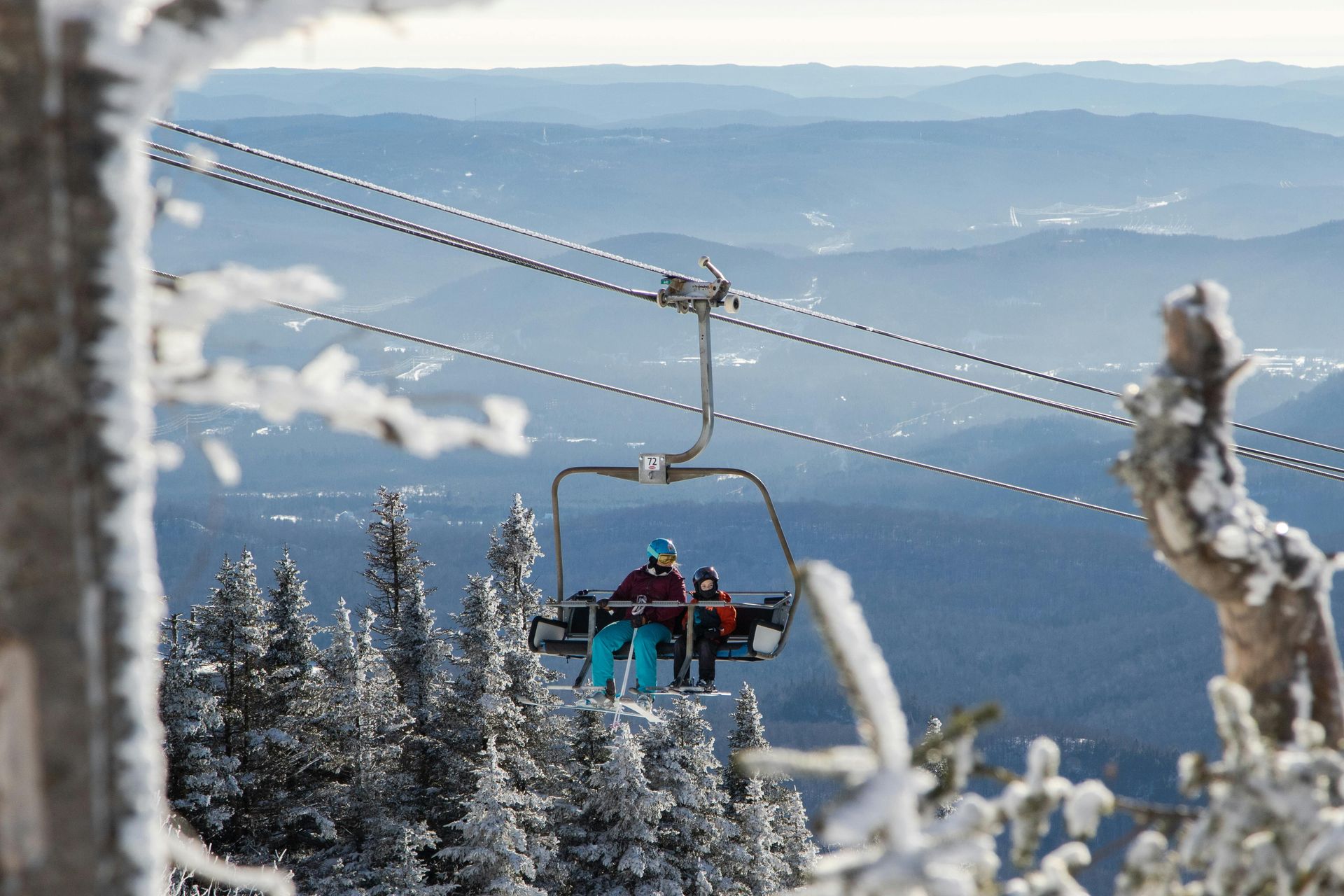 Ski lift carrying riders above snow-covered trees with blue mountains in the distance