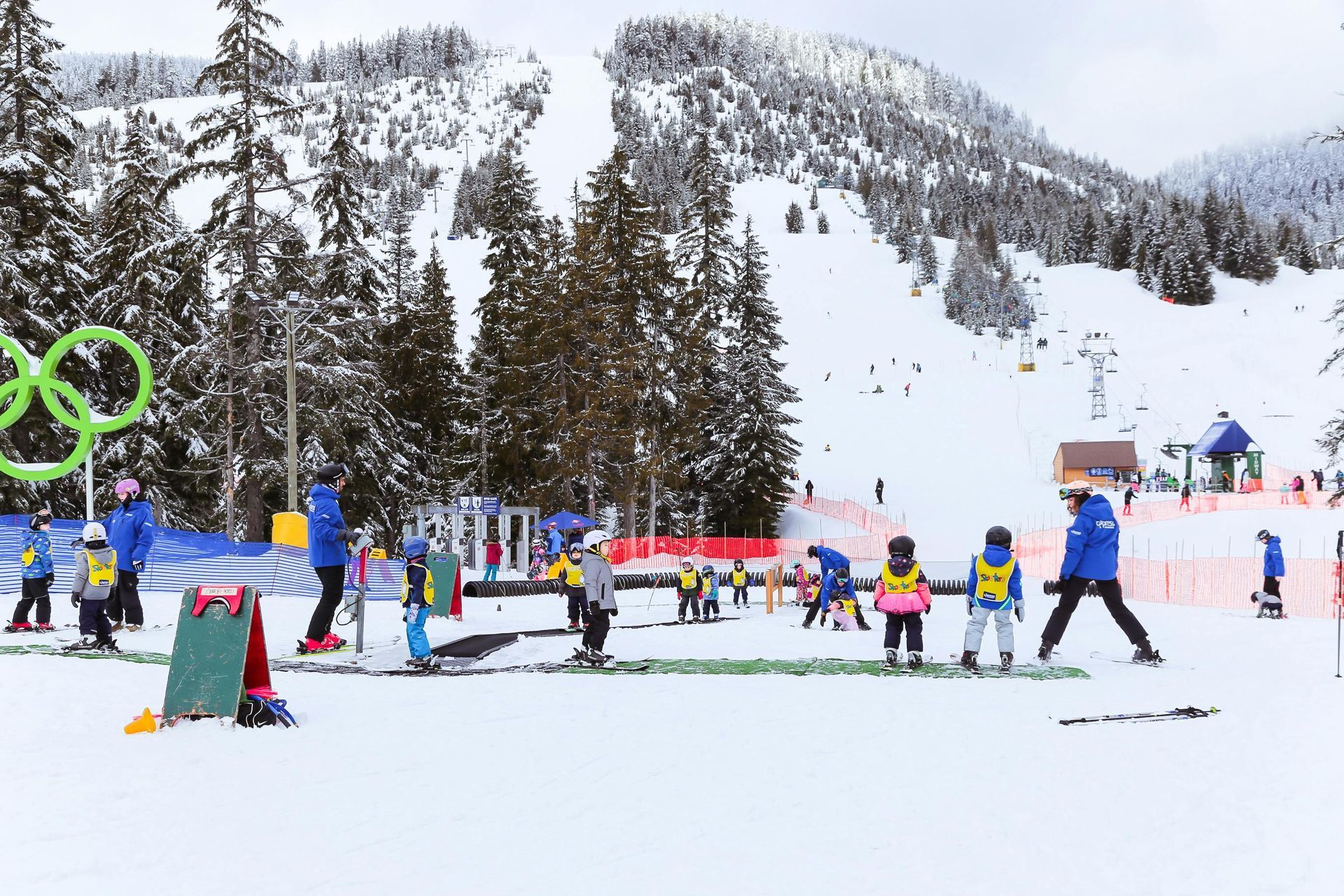 Ski school children in colorful gear learning on a snowy slope with mountains and trees in the background