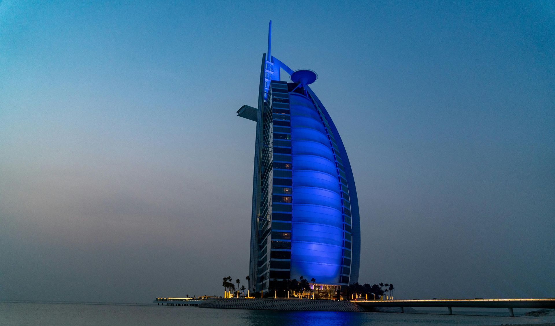 Blue-lit Burj Al Arab hotel at dusk by the sea