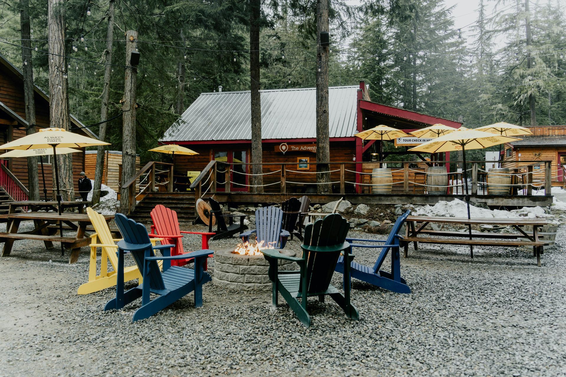 Colorful Adirondack chairs and picnic tables outside a rustic cabin in a wooded park setting.