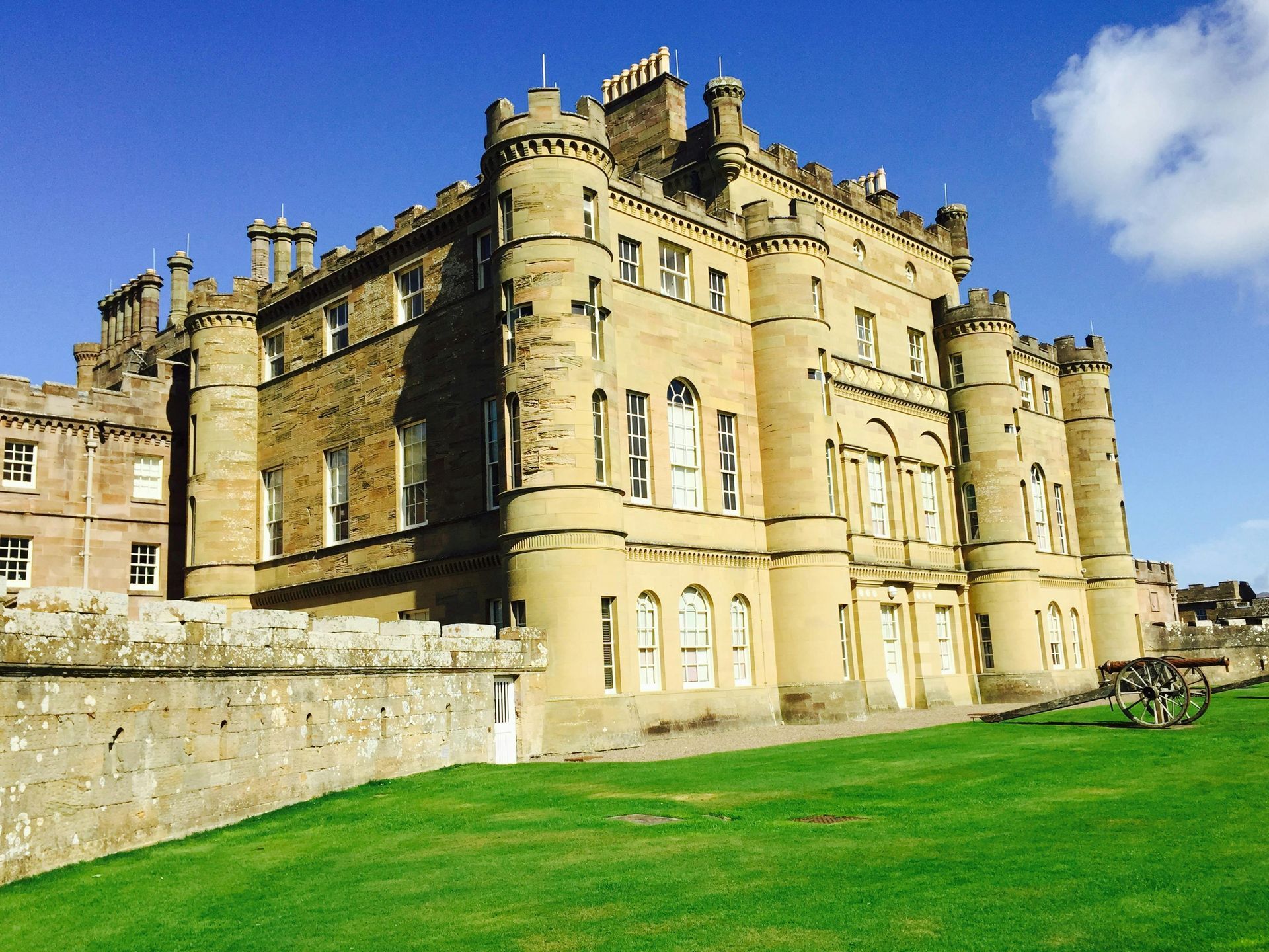 Large stone castle with towers and battlements on a grassy lawn under a clear blue sky