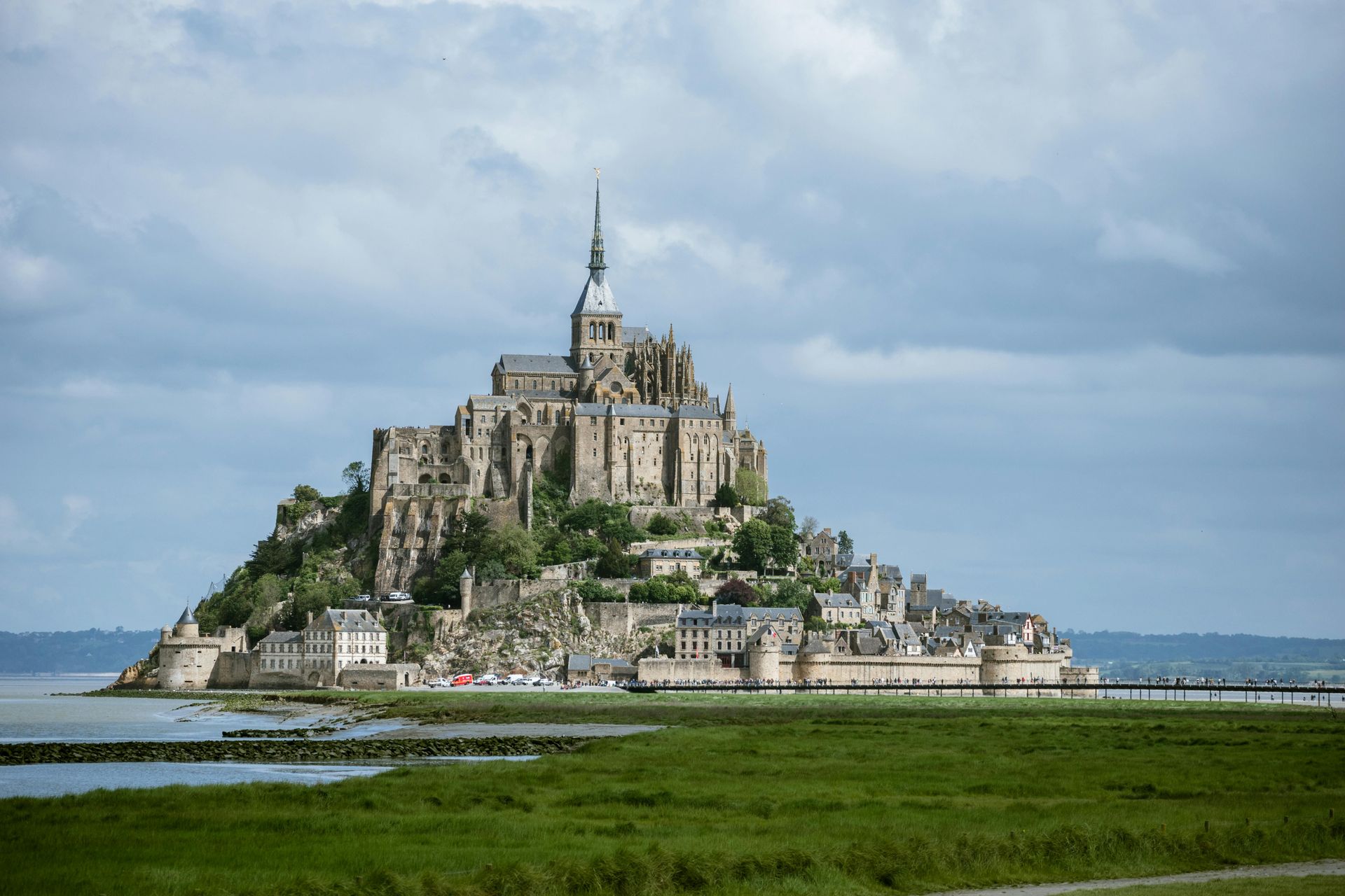 Mont Saint-Michel island abbey rising above tidal flats under a cloudy sky