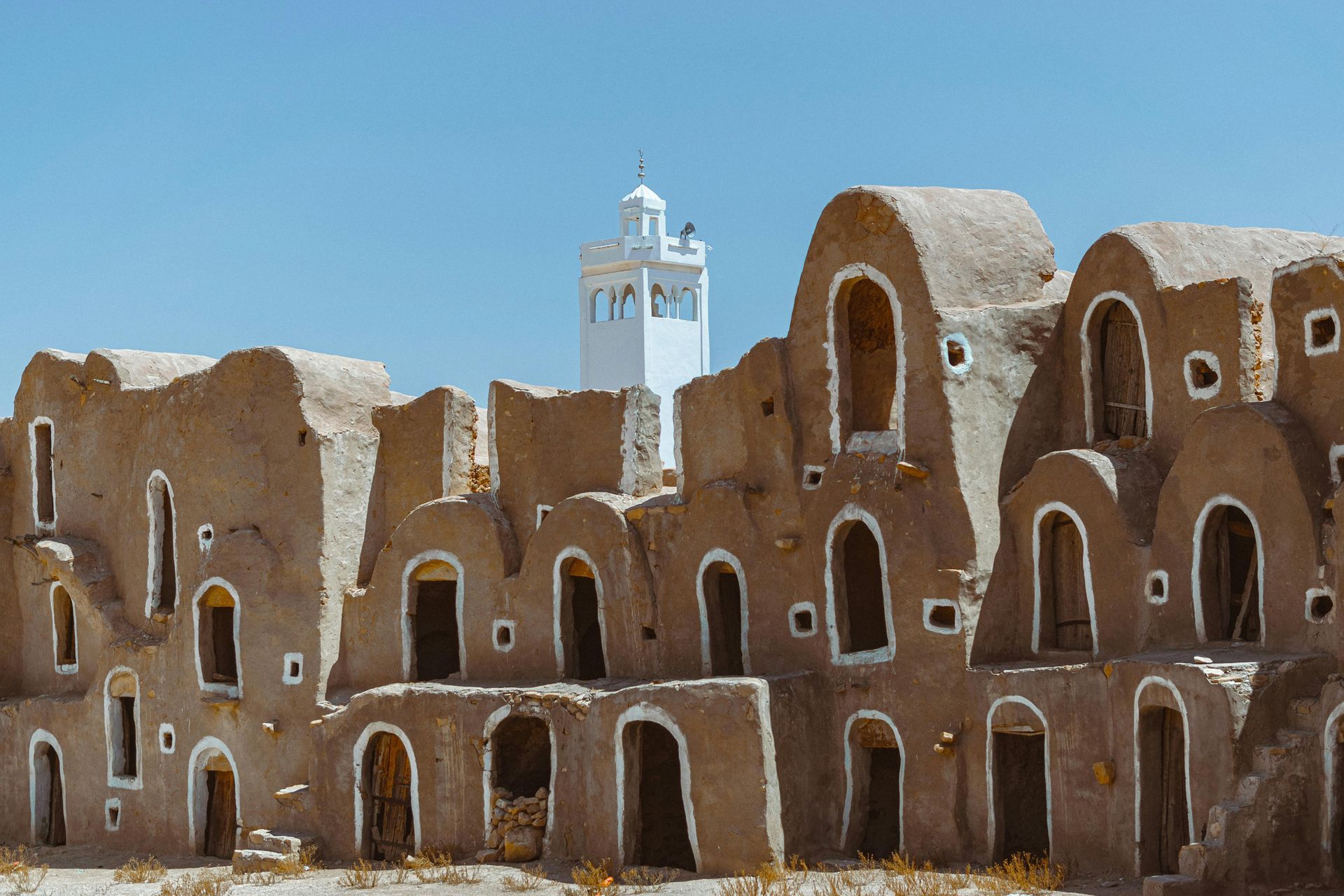 Ancient adobe ruins with arched openings and a white tower against a blue sky