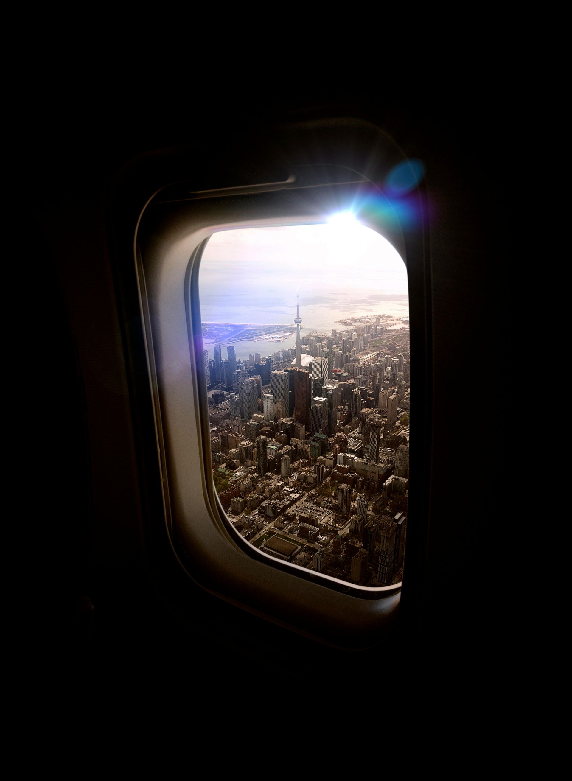 View through an airplane window of a city skyline at sunrise, with bright glare and clouds.