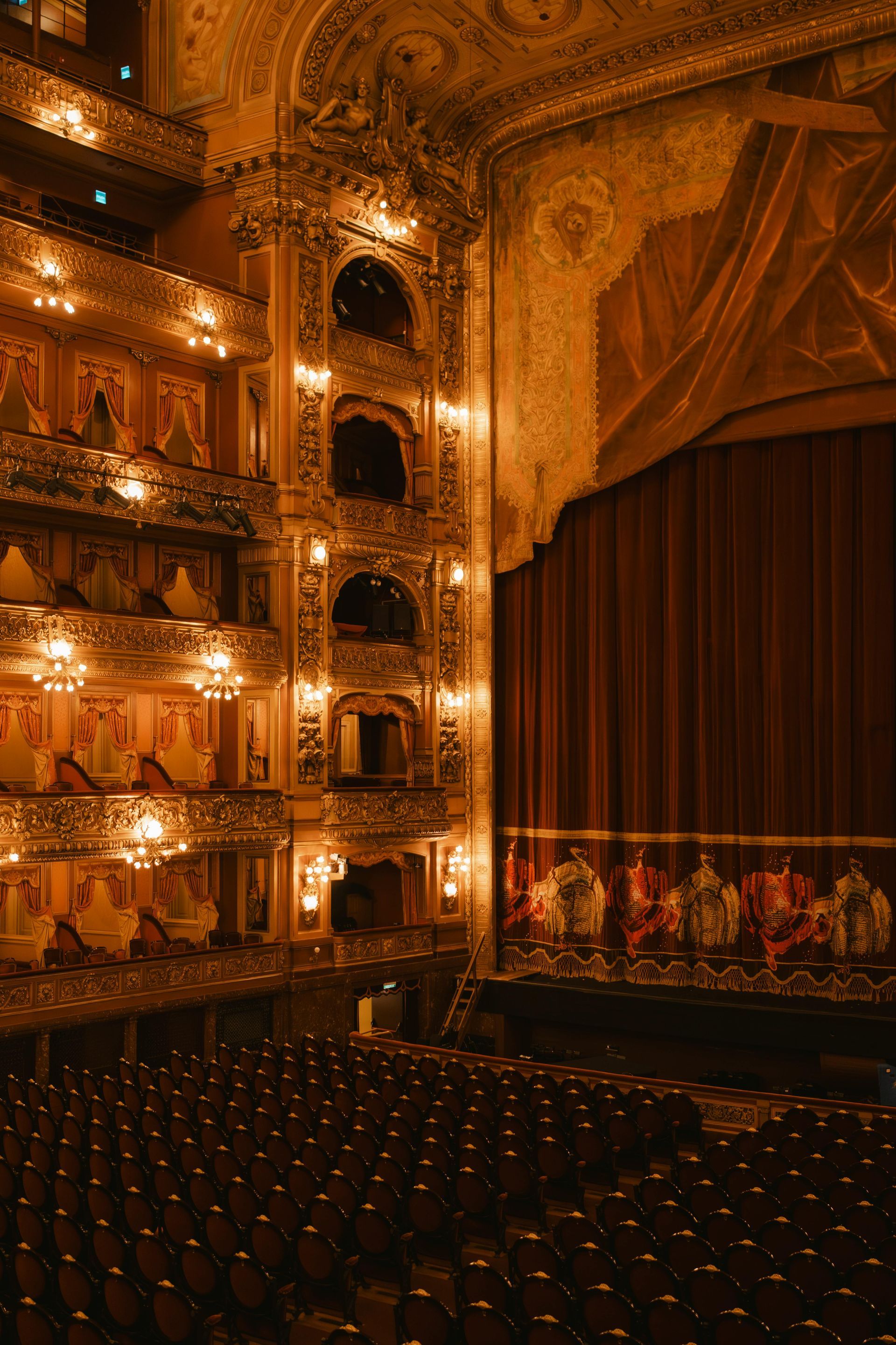 Ornate gold theater interior with balconies and a dark stage curtain above empty seating