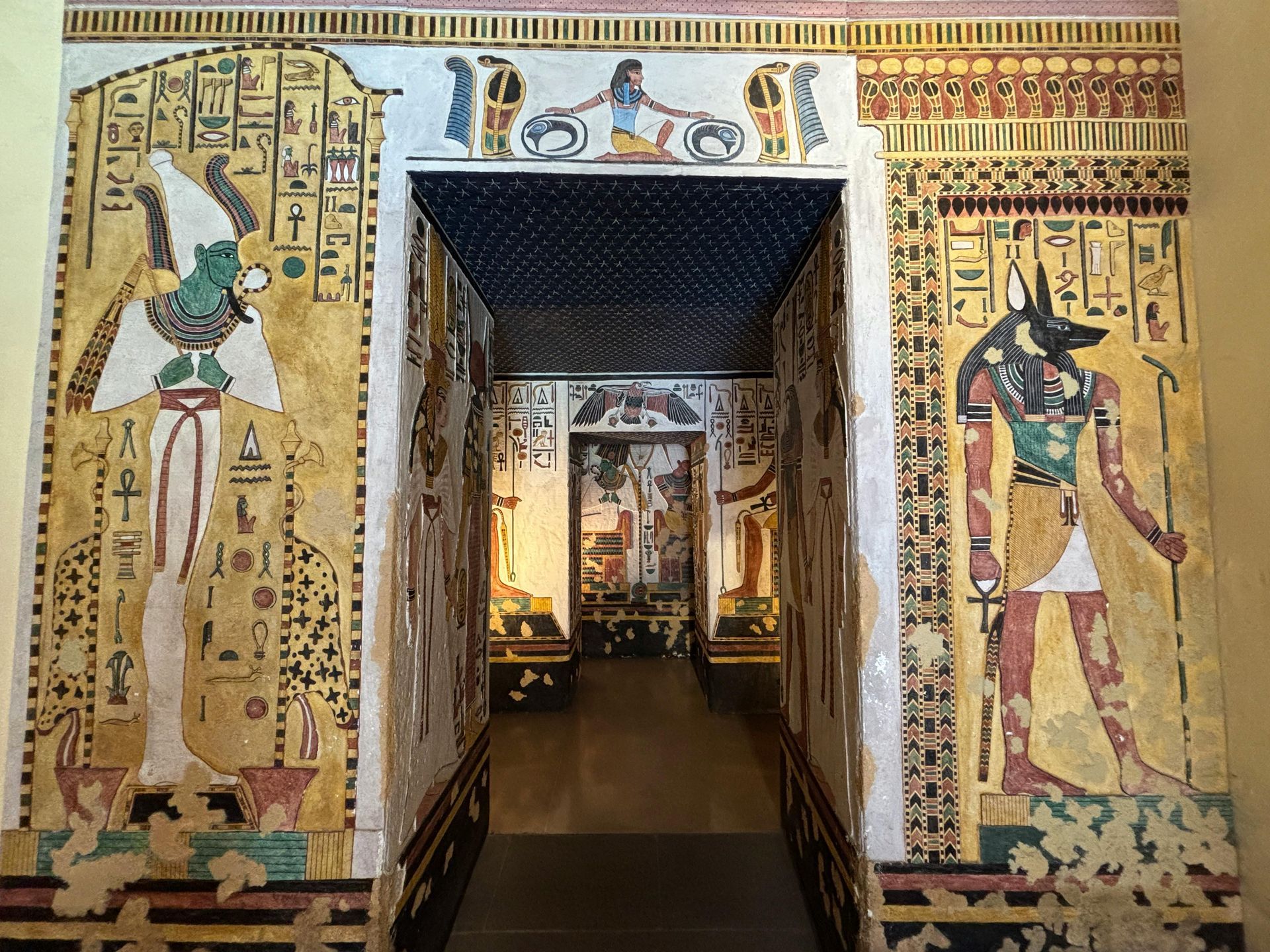 Ancient Egyptian temple entrance with colorful wall murals and hieroglyphs flanking a dim corridor