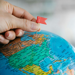 Hand placing a small red flag on a colorful globe map