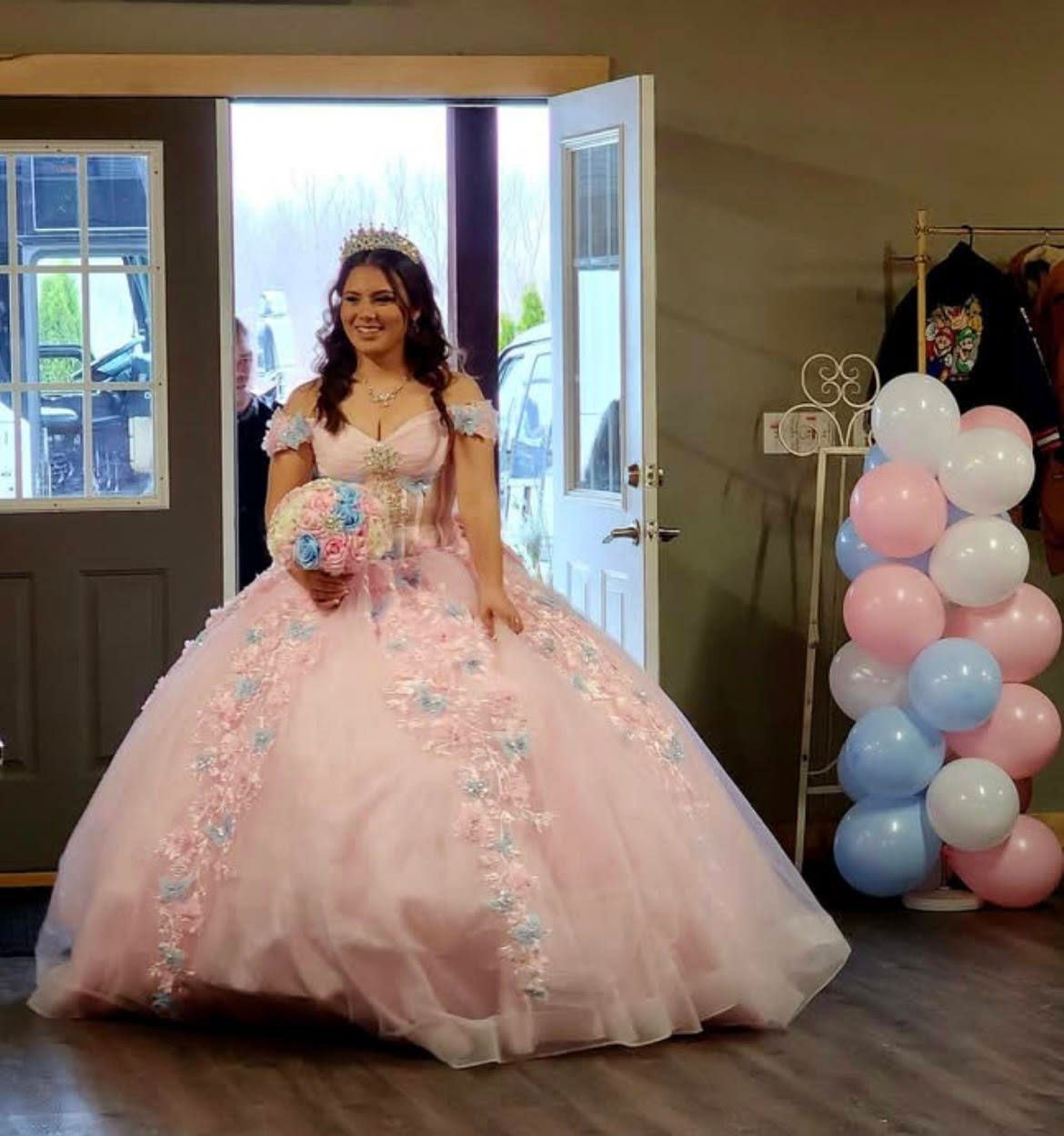 A woman in a pink dress is standing in front of a door holding a bouquet of flowers.