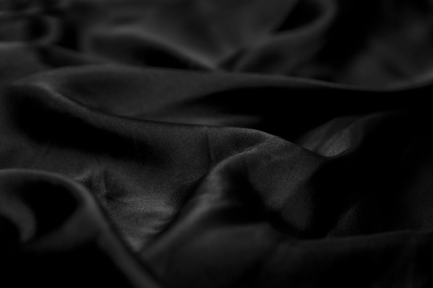 Dunkle Nahaufnahme von zerknittertem schwarzem Stoff mit weichen Falten und Lichtreflexen