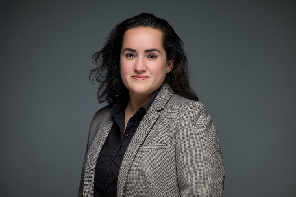 Woman in a striped blazer and black shirt smiles against a gray background.