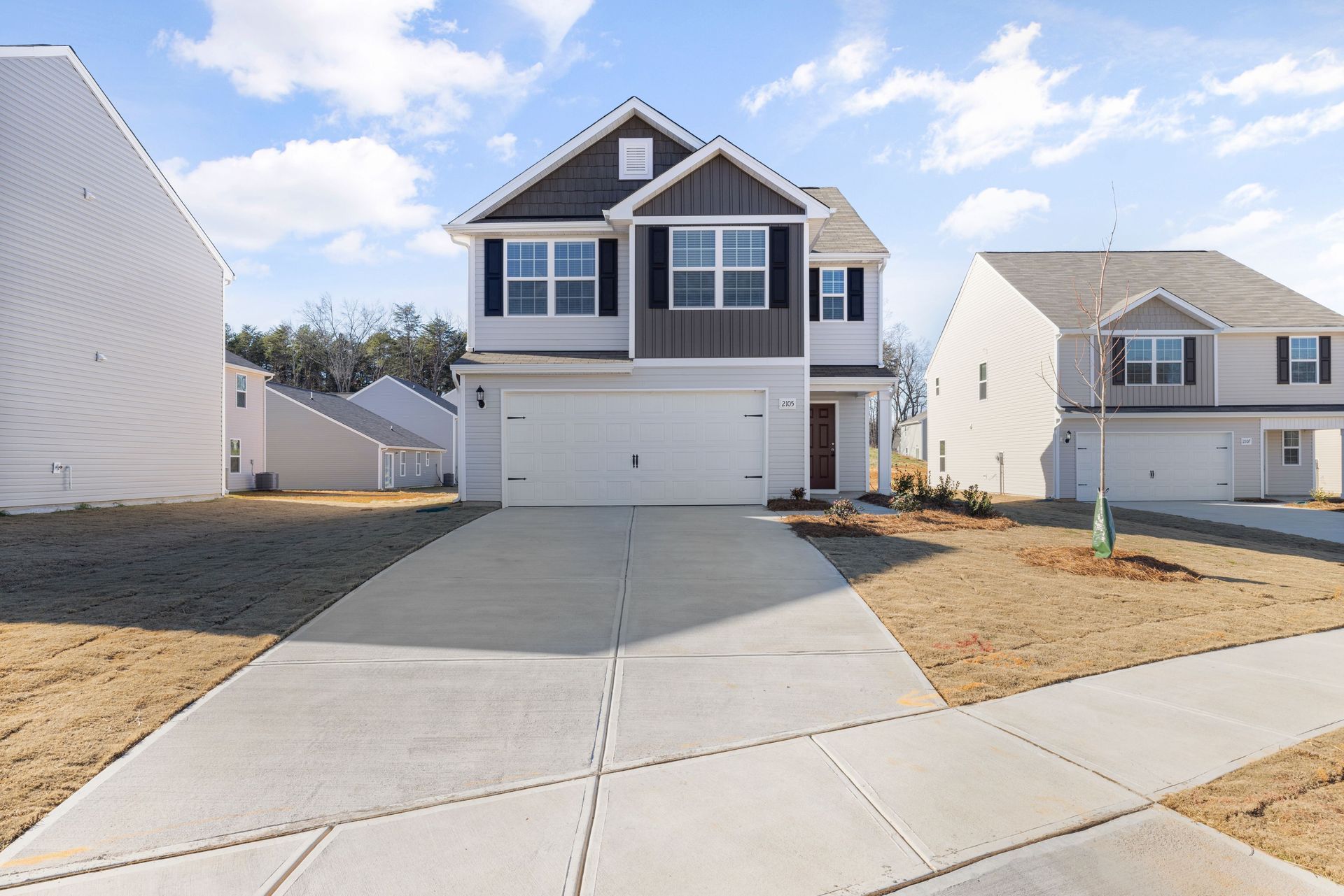 New suburban two-story house with a driveway and garage under a partly cloudy sky