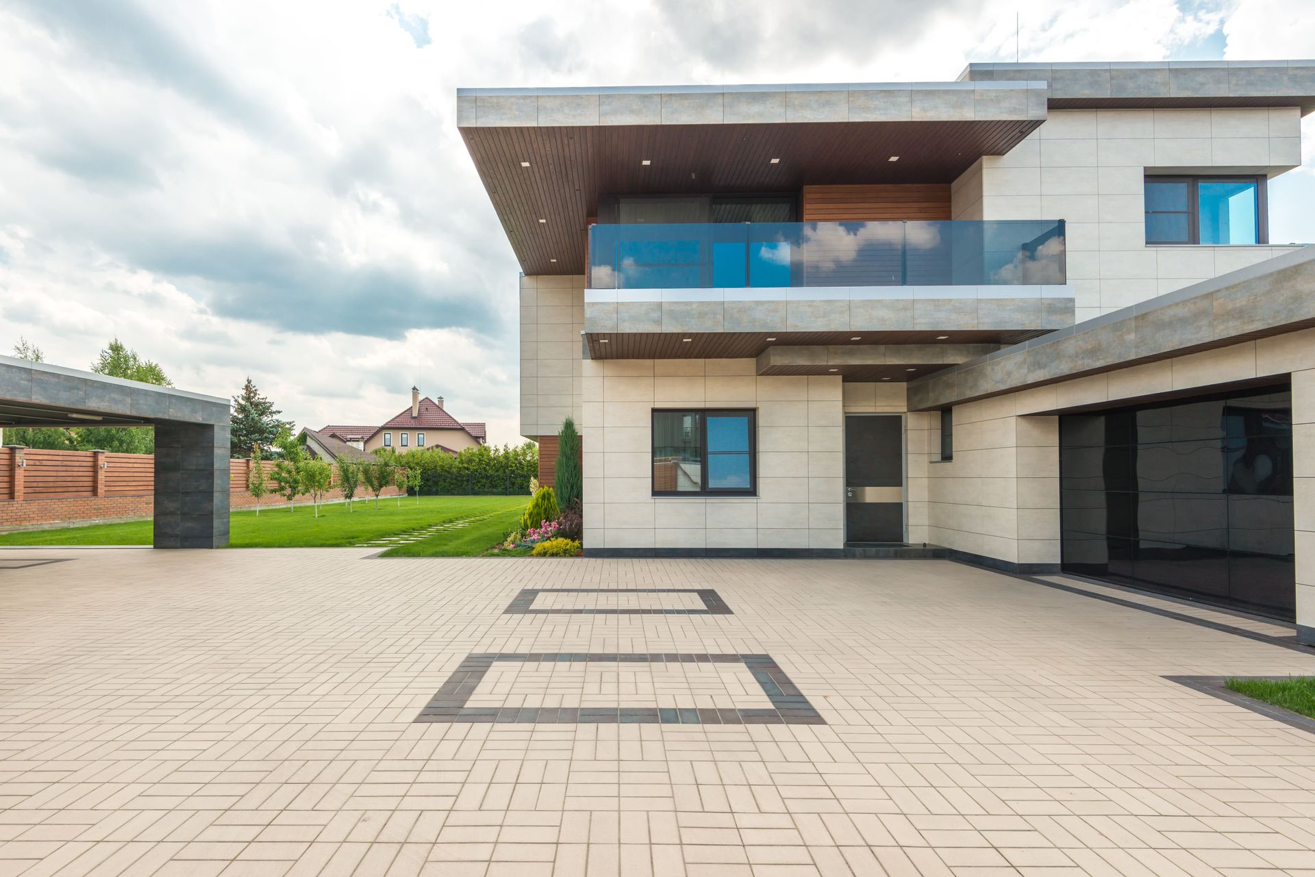 Modern two-story house with a driveway, garage, and large patio under a cloudy sky