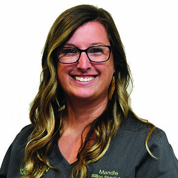 A woman wearing glasses and a scrub top is smiling for the camera.