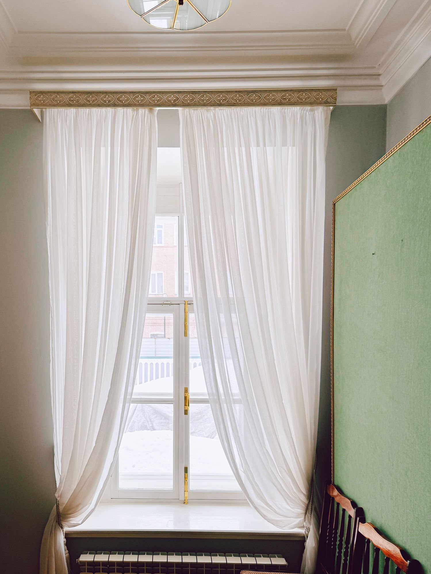A bedroom with a bed and a window with white curtains.