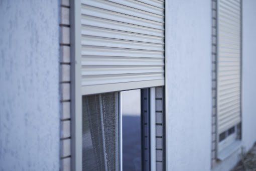 A white building with a window with a shutter on it.