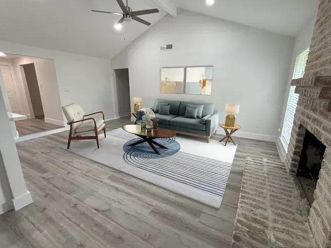 Bedroom with bed, armchair, rug, and open doorway to bathroom. Beige walls and light wood flooring.