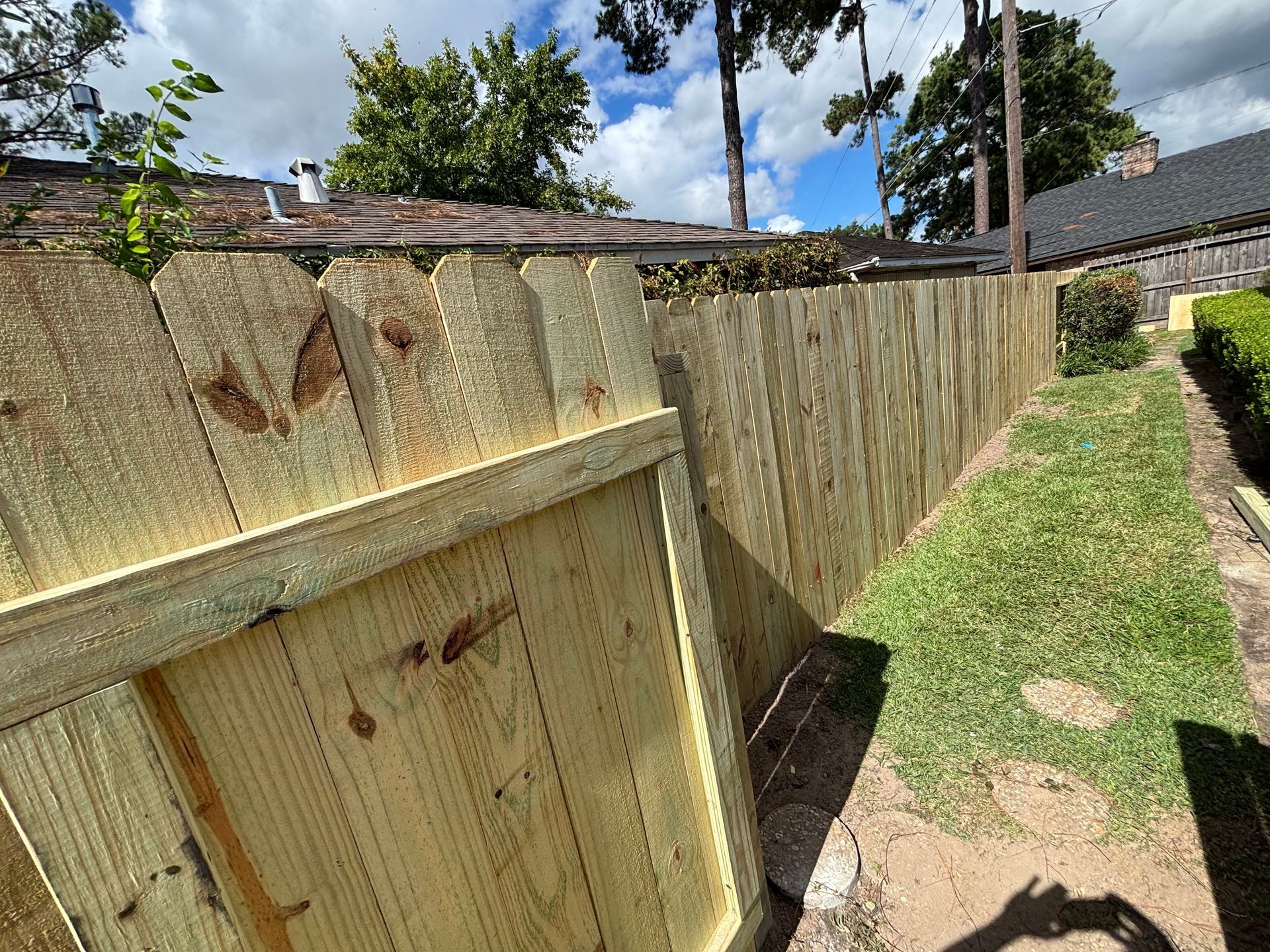 New wooden fence enclosing a yard with green grass and a small garden. Sunny, daytime.