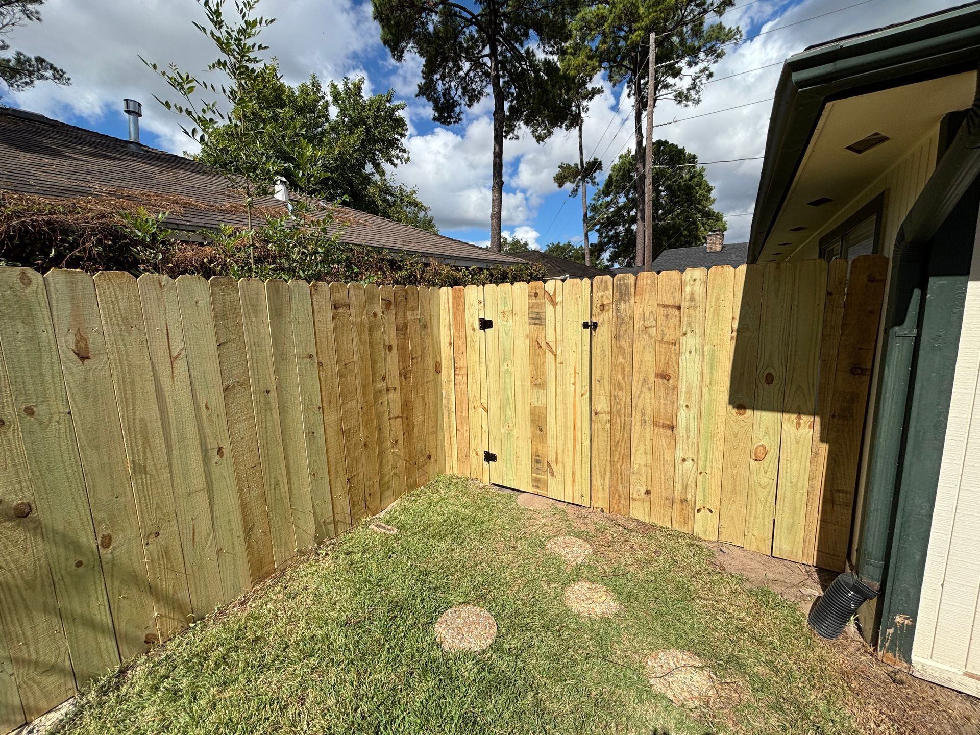 Wooden fence encloses a small backyard with green grass, stepping stones, and a gate.