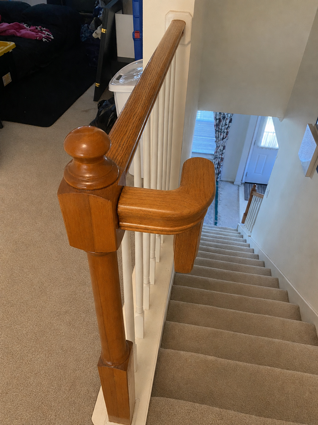 Wooden stair railing with white spindles beside a carpeted staircase leading downward