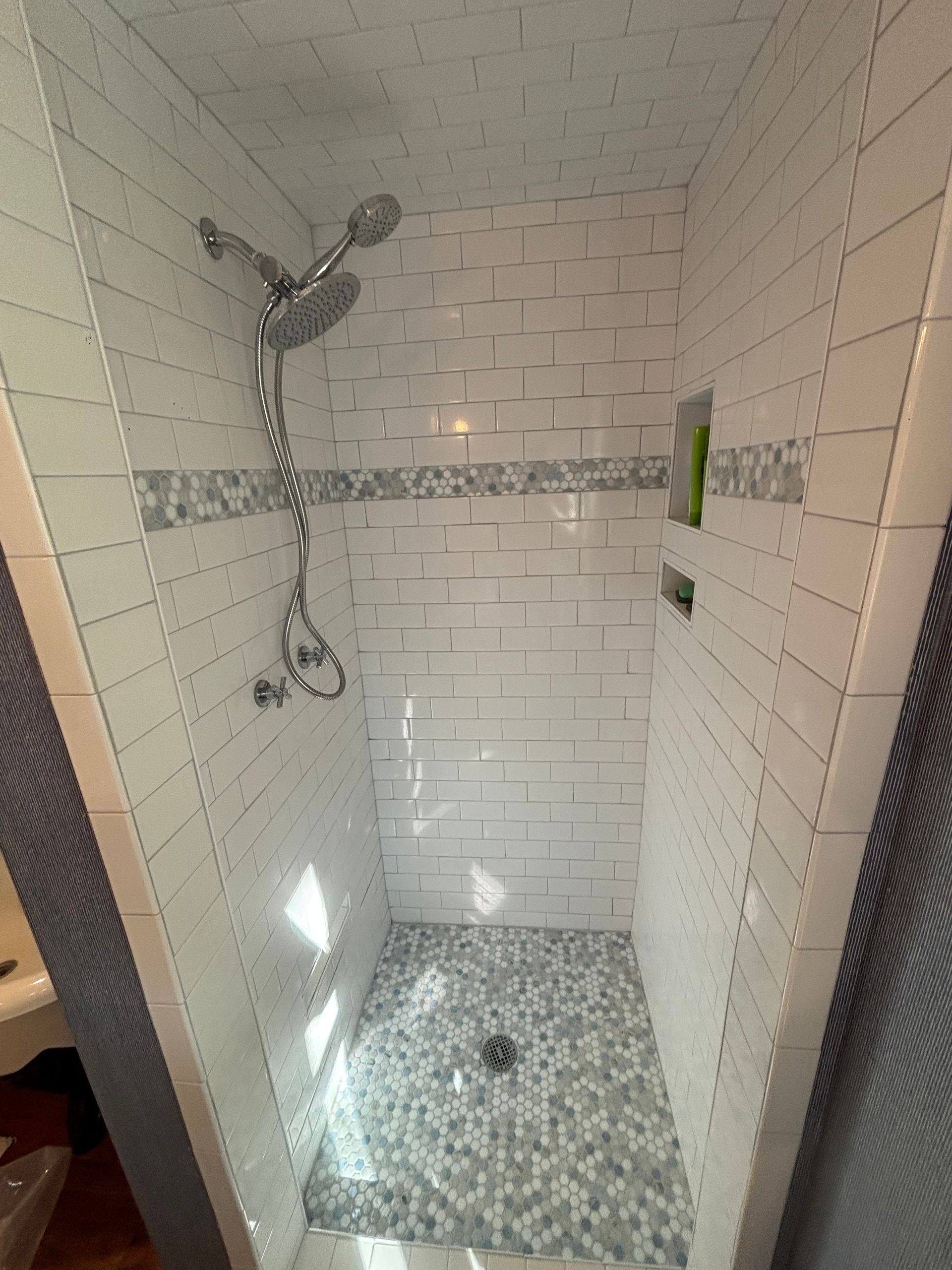 Shower stall with white subway tiles, pebble floor, and chrome showerhead.