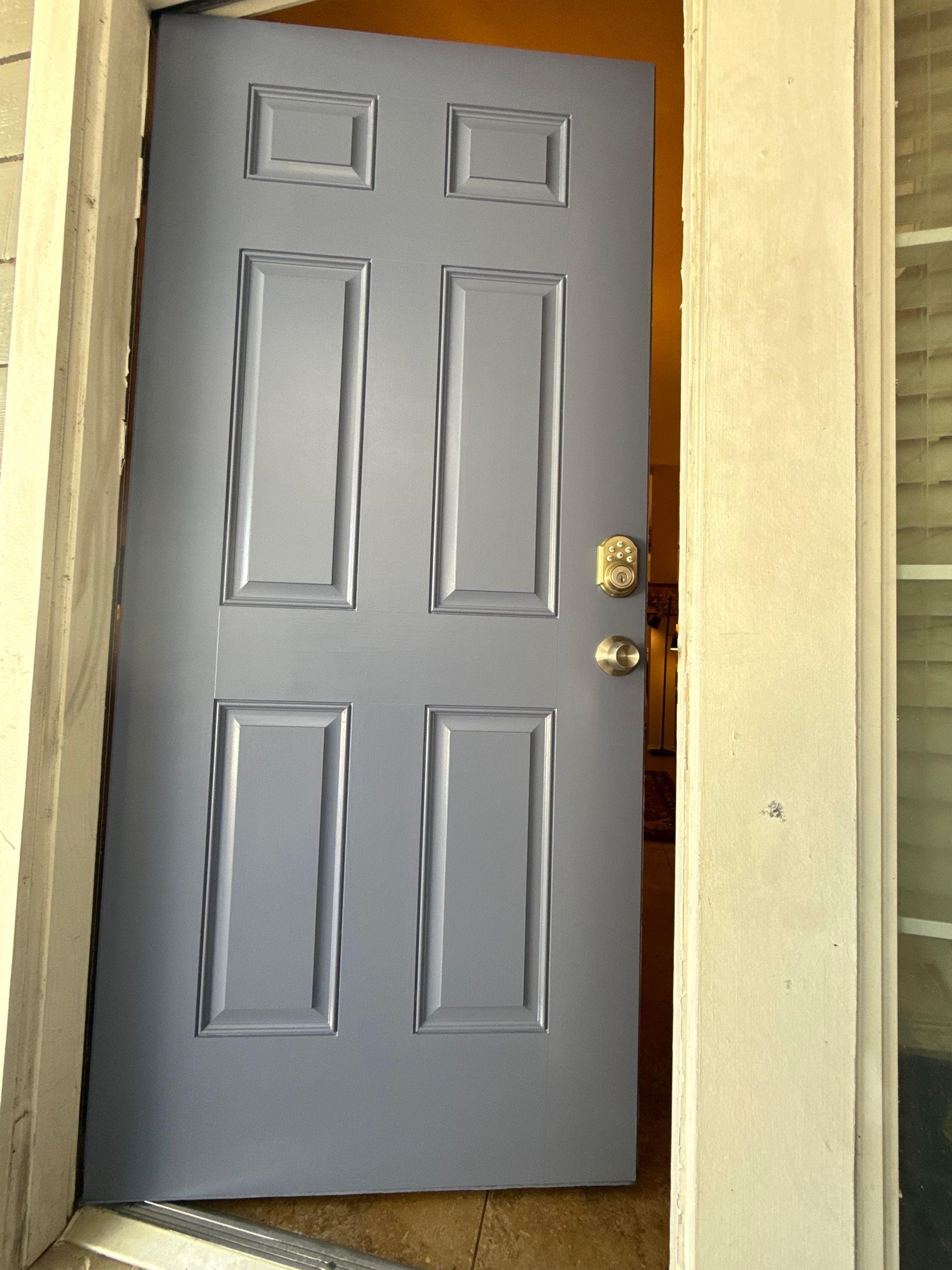Partially open gray front door with brass knob and white trim