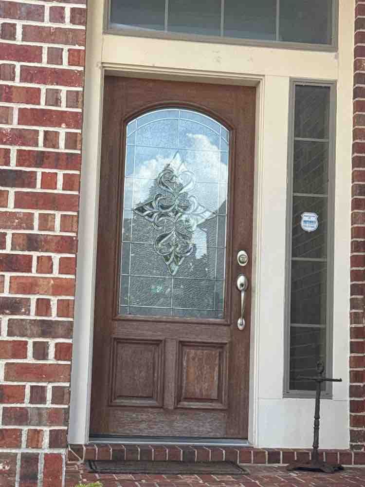 Brown front door with arched glass panel and side window, set in a brick and white trim frame.