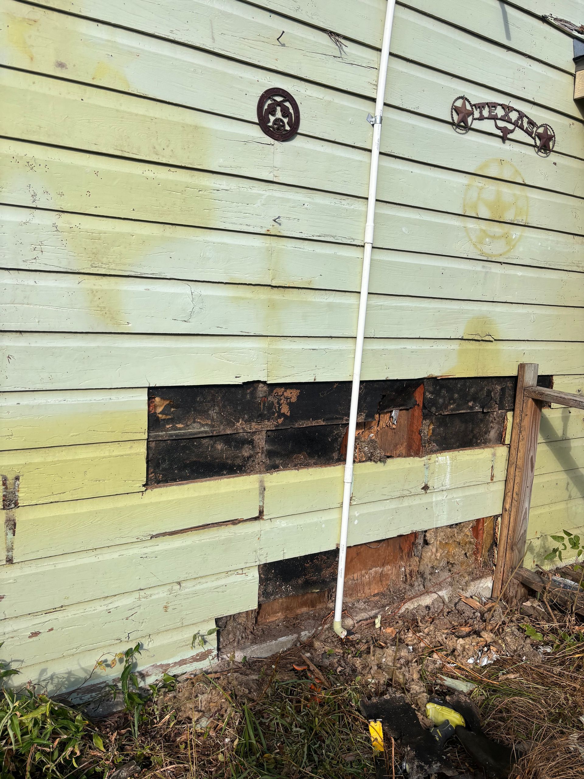 Exterior wall with damaged wooden siding, showing exposed dark wood and light green paint.