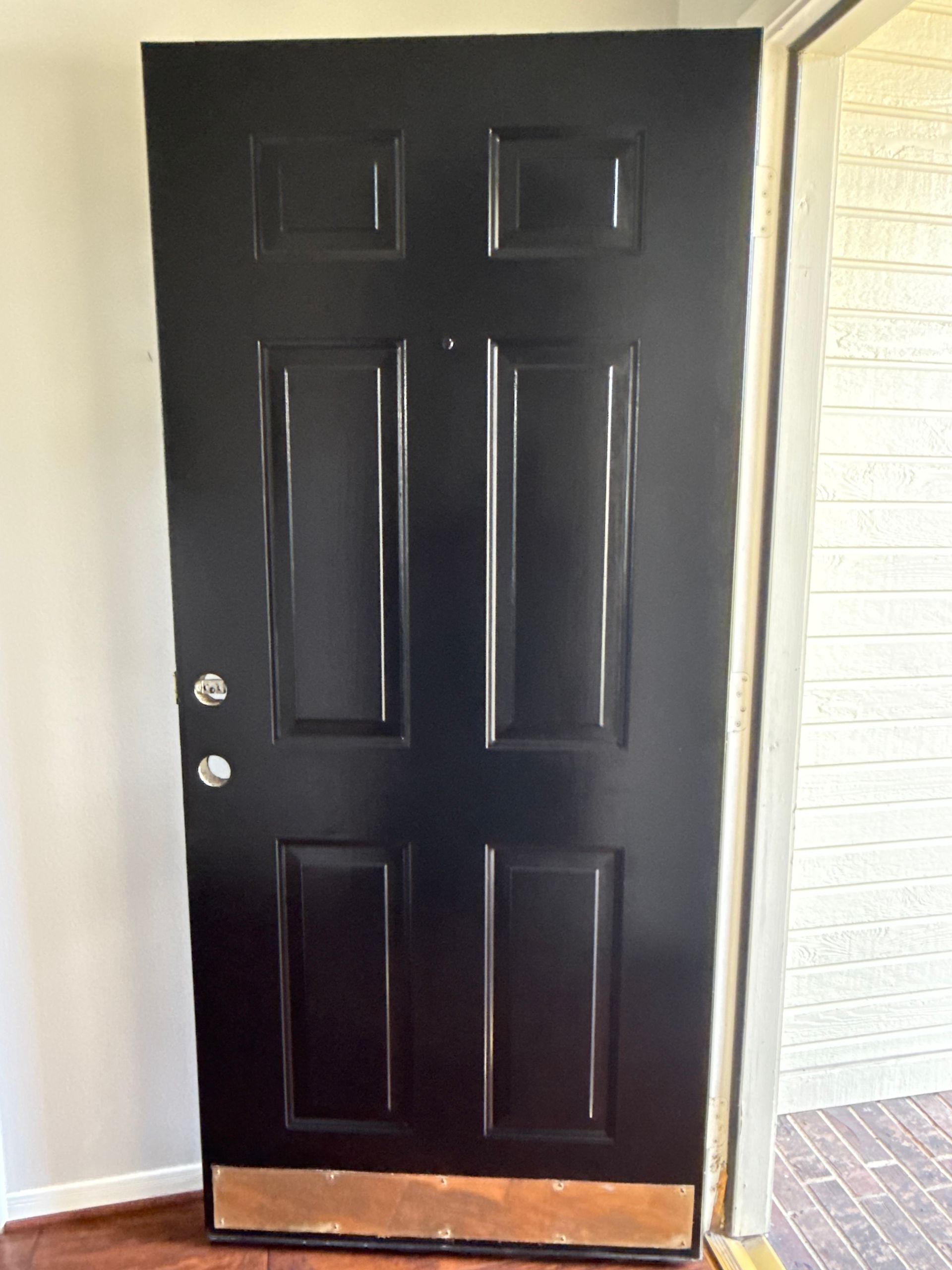 Black front door with silver knob, against a white brick wall and porch floor.